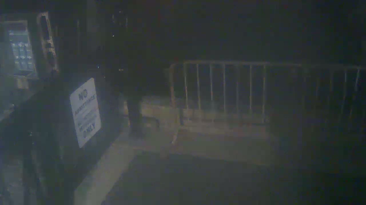 A person walks past a metal barricade at night in a dimly lit area.