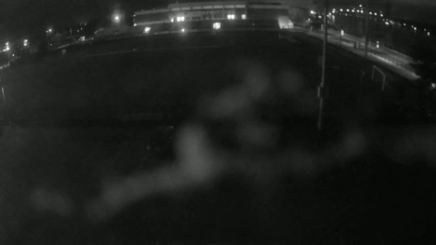 A blurry nighttime view shows a dark, wet surface reflecting lights from a building in the distance.