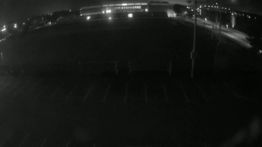 A nighttime, low-light view shows an empty parking lot with a building and road visible in the distance.