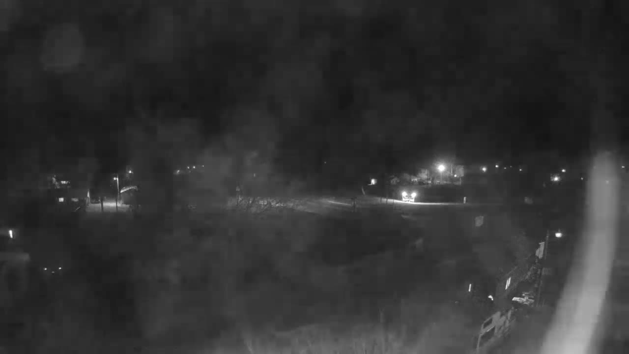 A blurry, monochromatic image depicts a foggy night street scene with a vehicle's bright headlights illuminating the foreground, complemented by scattered distant streetlights.