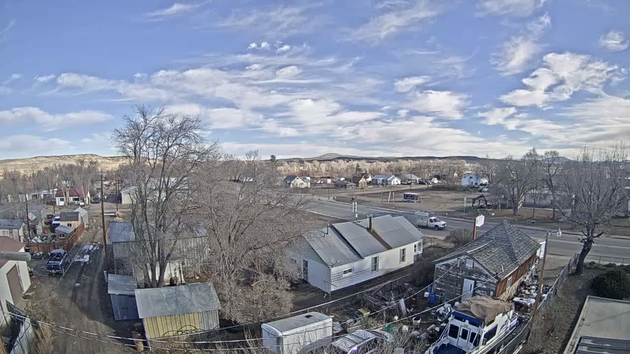 A snow-covered residential area is seen from an elevated perspective at night under a cloudy sky, with streetlights casting light on the houses and bare trees.
