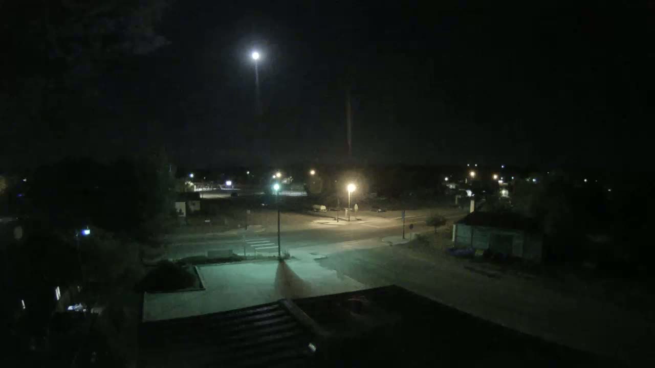 A nighttime view of a residential street intersection, illuminated by streetlights under a mostly clear sky with a bright moon.