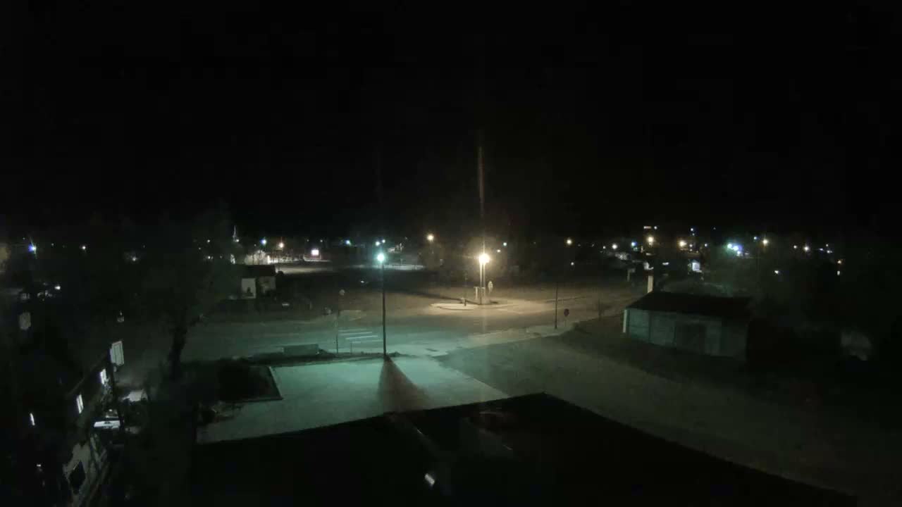 An elevated view captures a snow-covered town at night, with streetlights illuminating the freshly fallen snow on roads and rooftops under cold, clear skies.