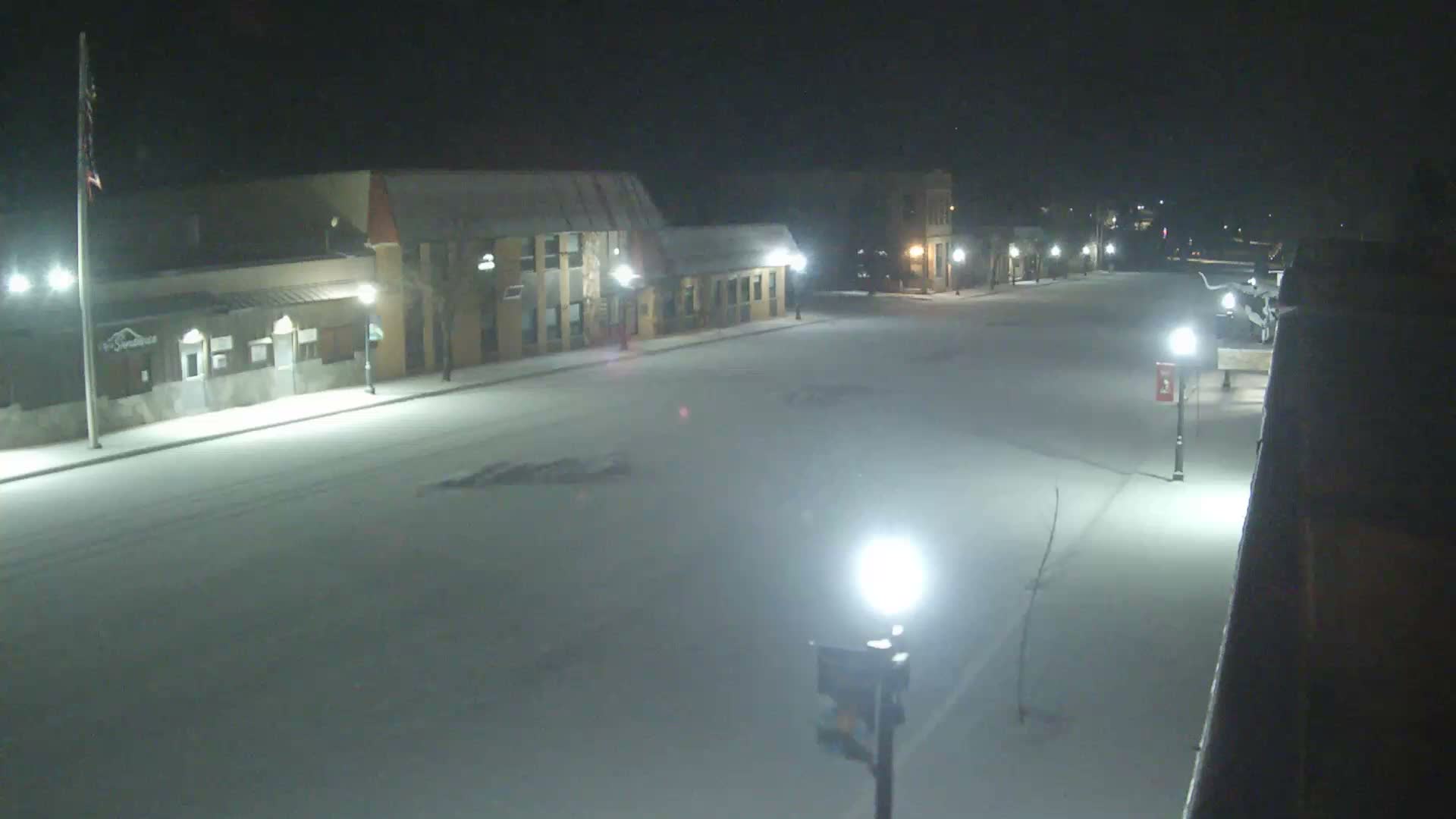 A snow-covered street lined with illuminated buildings and streetlights stretches into the distance on a dark, snowy night.
