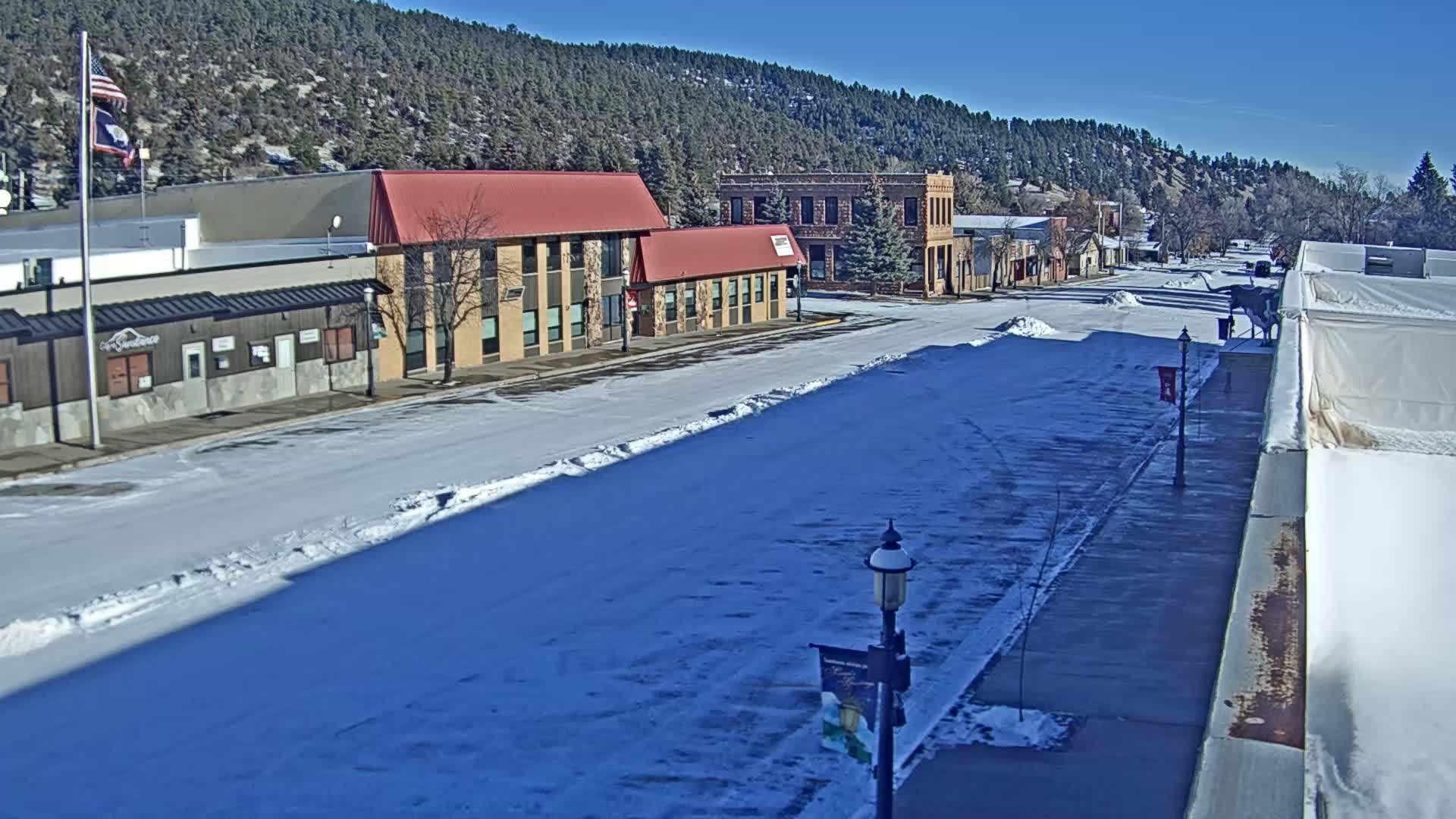 An empty street at night is illuminated by bright streetlights and the glowing windows of buildings lining both sides, with patches of ice and melted snow visible on the ground.