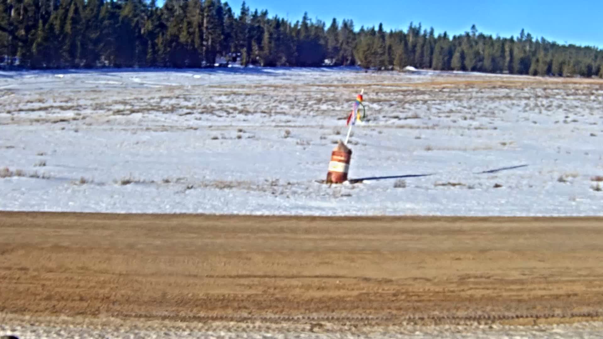 A dark, grainy, and blurry image shows a snow-covered field under dim, overcast skies, with a faint dark shape standing in the distant center before a dark, blurry horizon.