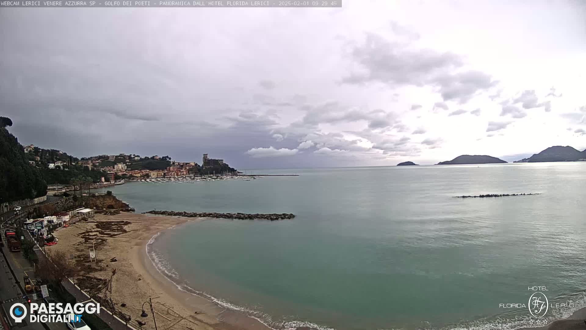 A coastal town with a sandy beach and calm sea is viewed under an overcast sky.