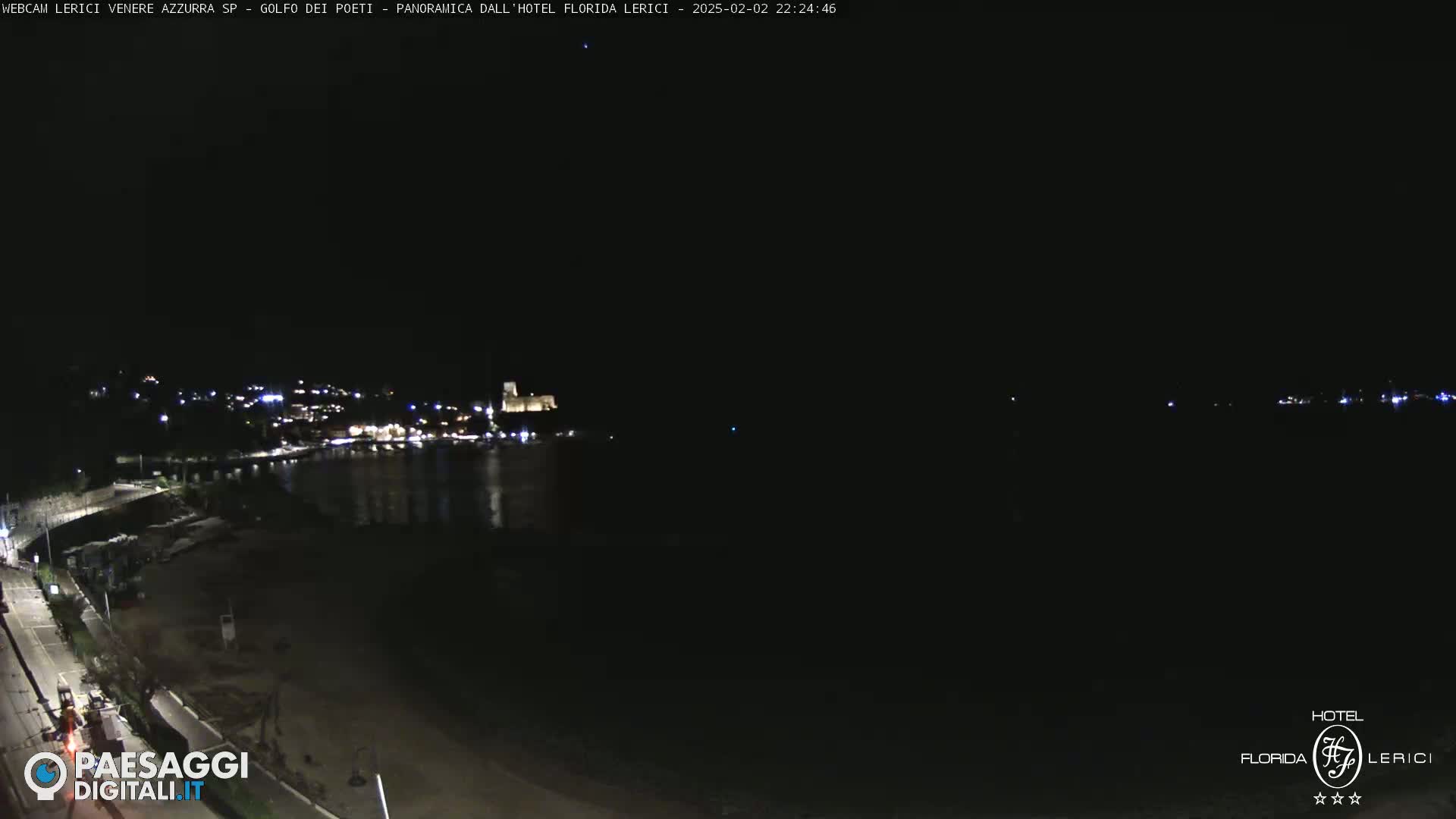 A nighttime, long-range view shows a dark body of water with a dimly lit town and shoreline in the distance.