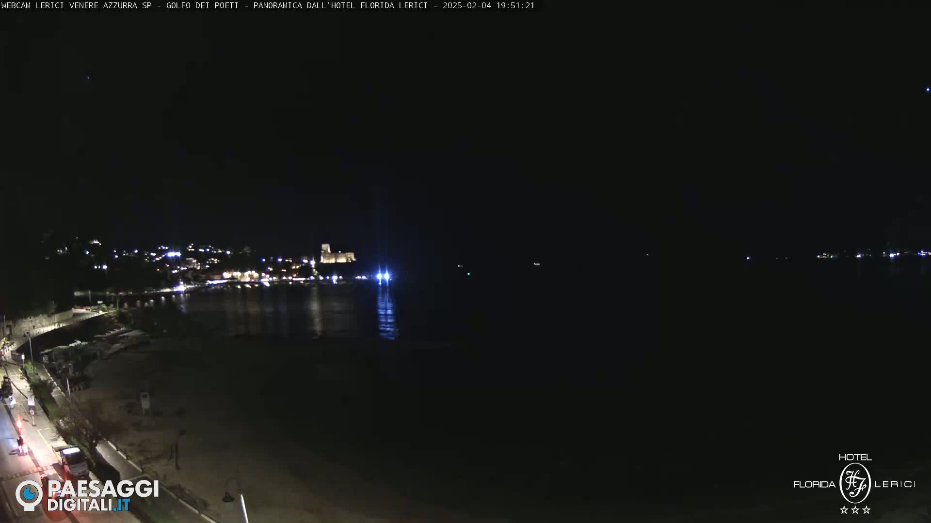A nighttime view of a dark, calm body of water with a dimly lit shoreline and buildings in the distance.