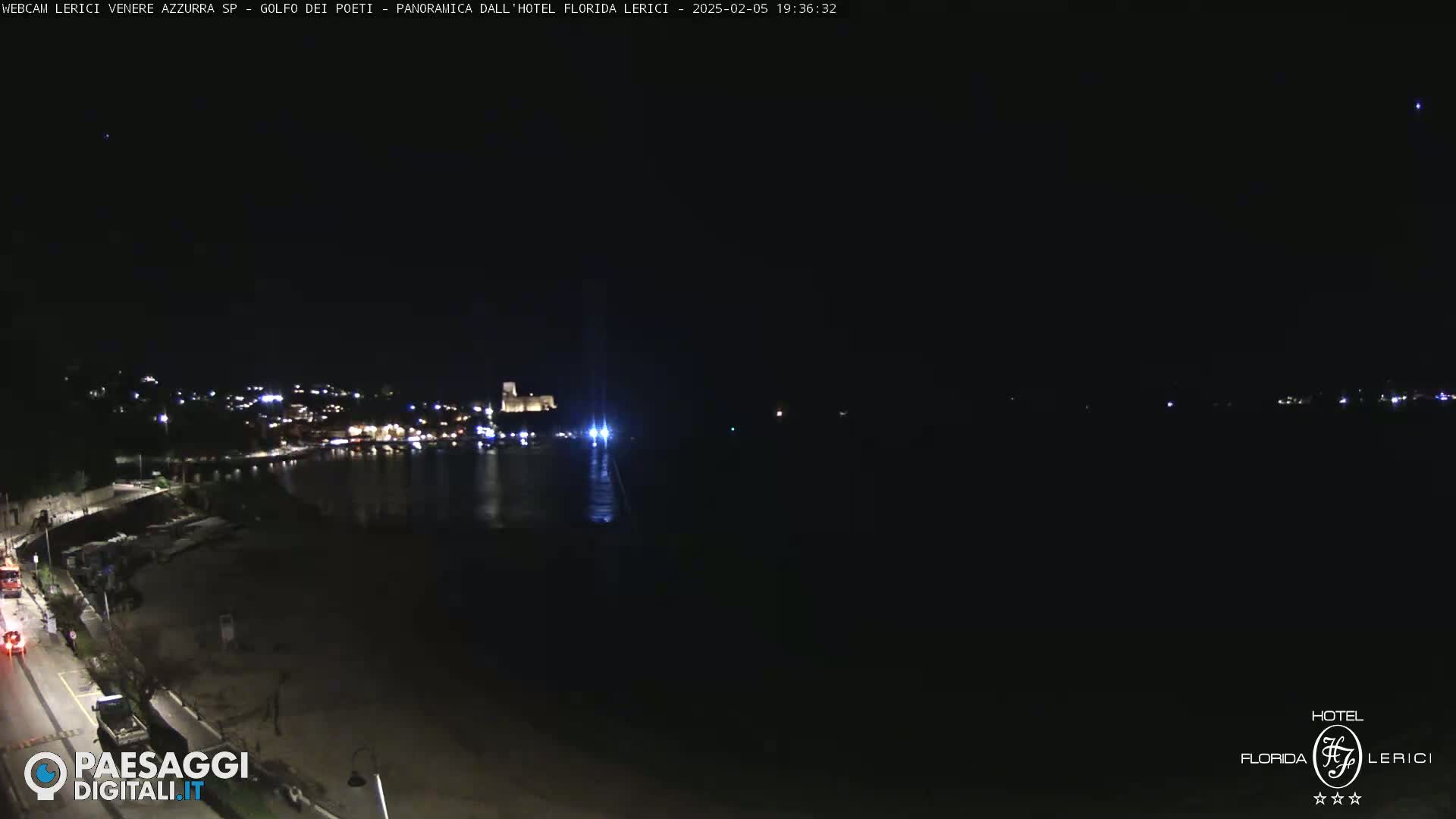 A nighttime view of a dark coastline with a few lights visible in the distance across a body of dark water.