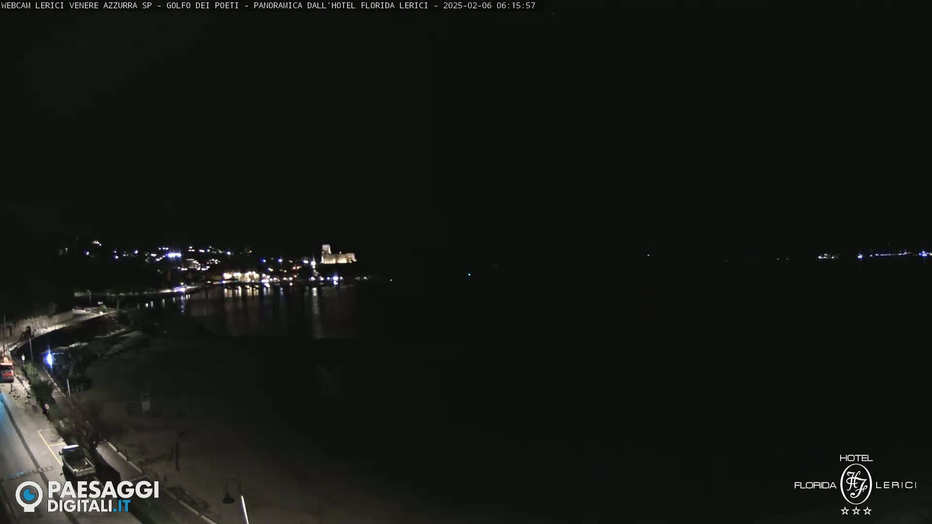 A nighttime, long shot of a dark, calm body of water with a dimly lit town on the far shore.