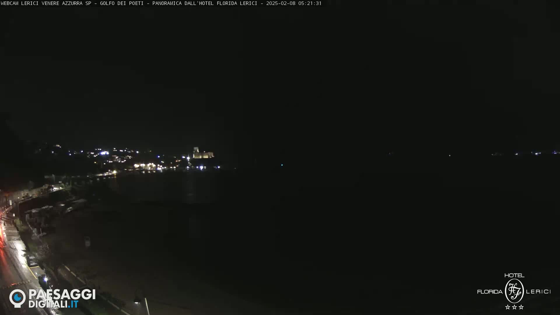 A nighttime, dark view of a coastal town with faint lights visible across a dark body of water.