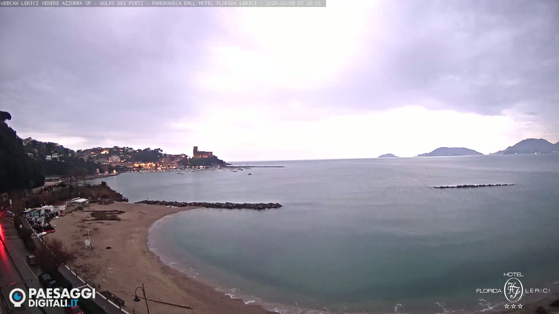 A coastal town with a sandy beach and calm sea is visible under an overcast sky.