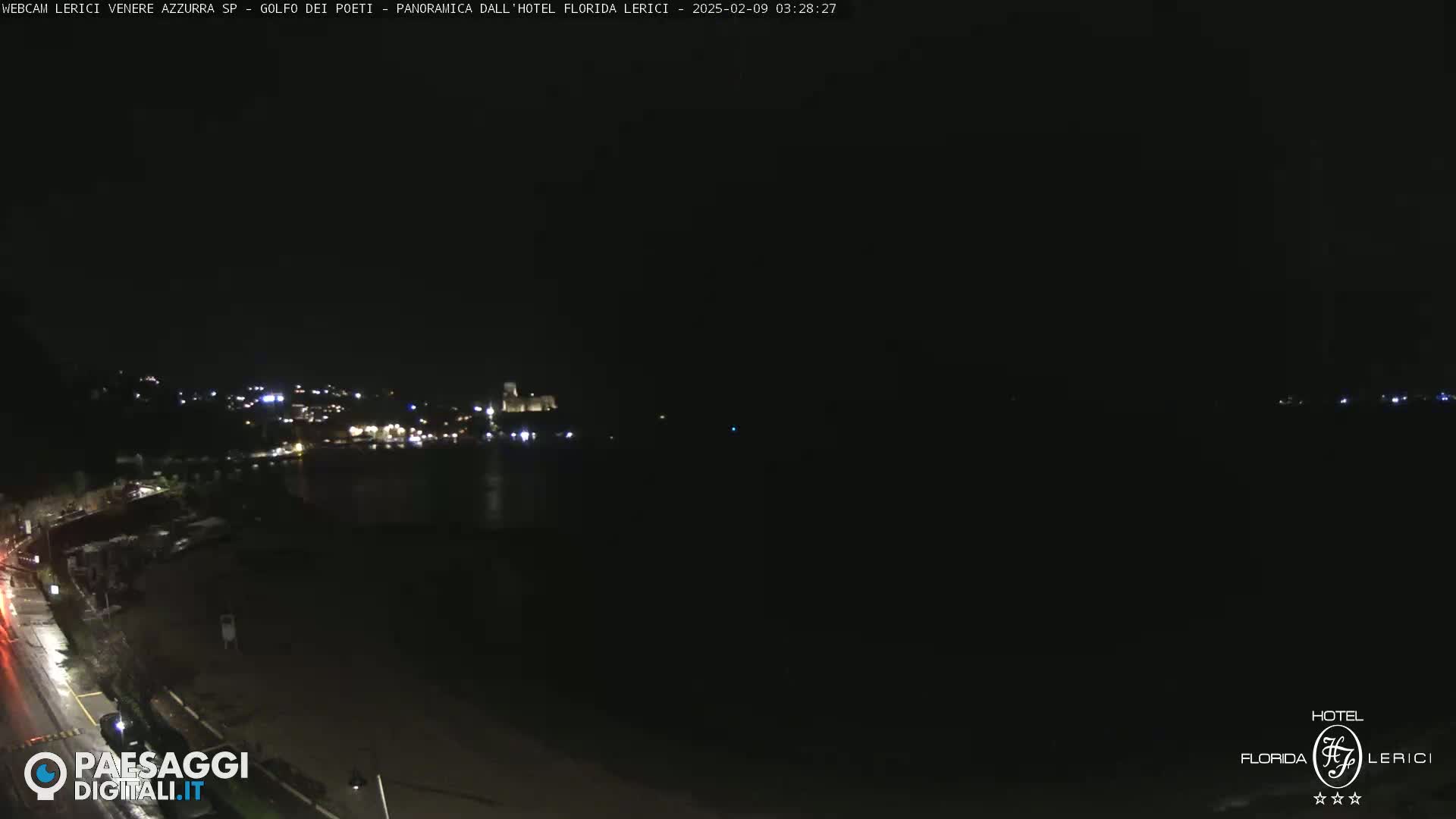 A nighttime, dark view of a coastline with dimly lit buildings and a body of dark water.