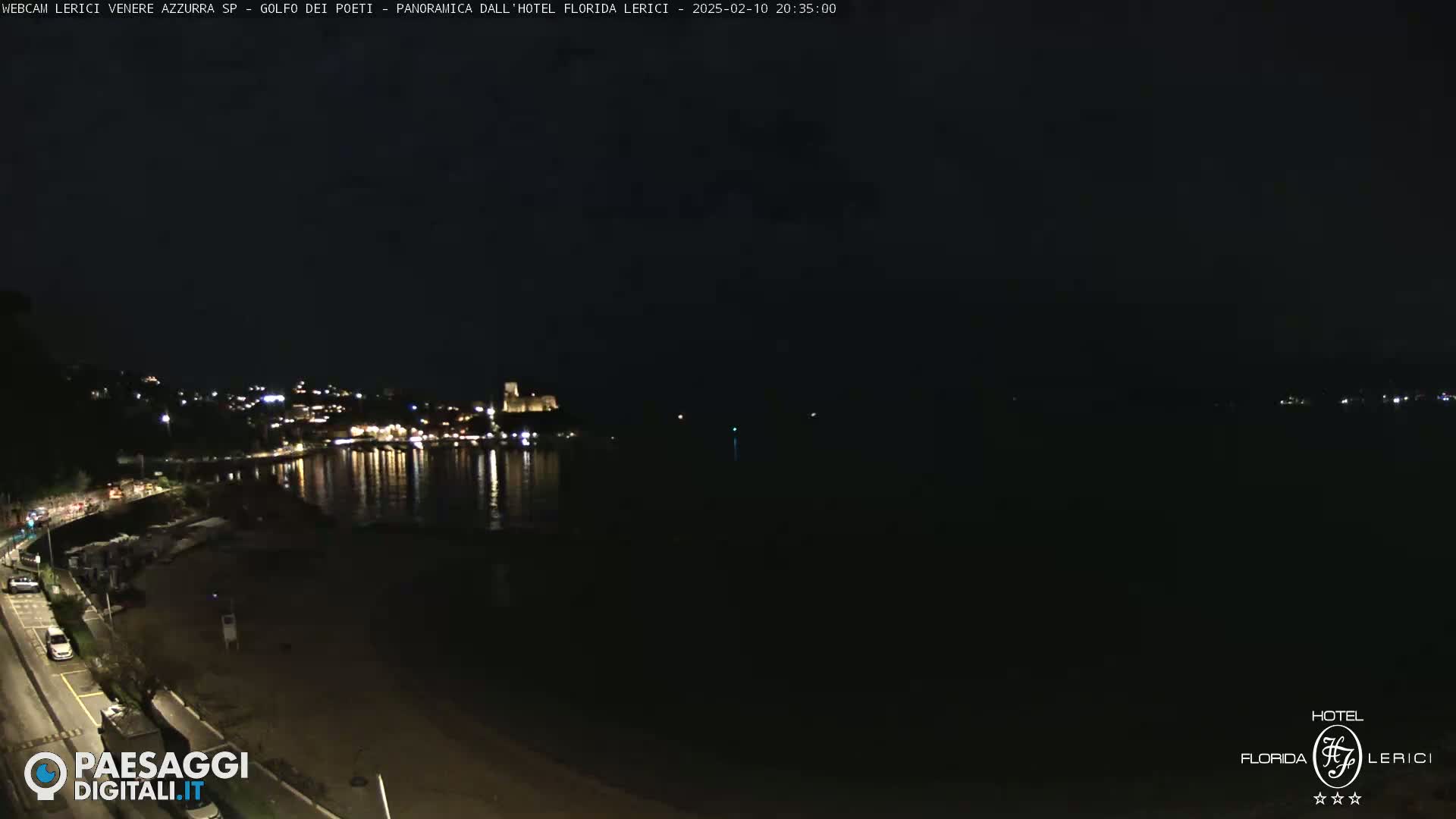 A nighttime view of a dark, calm body of water reflecting the lights of a town on the opposite shore.