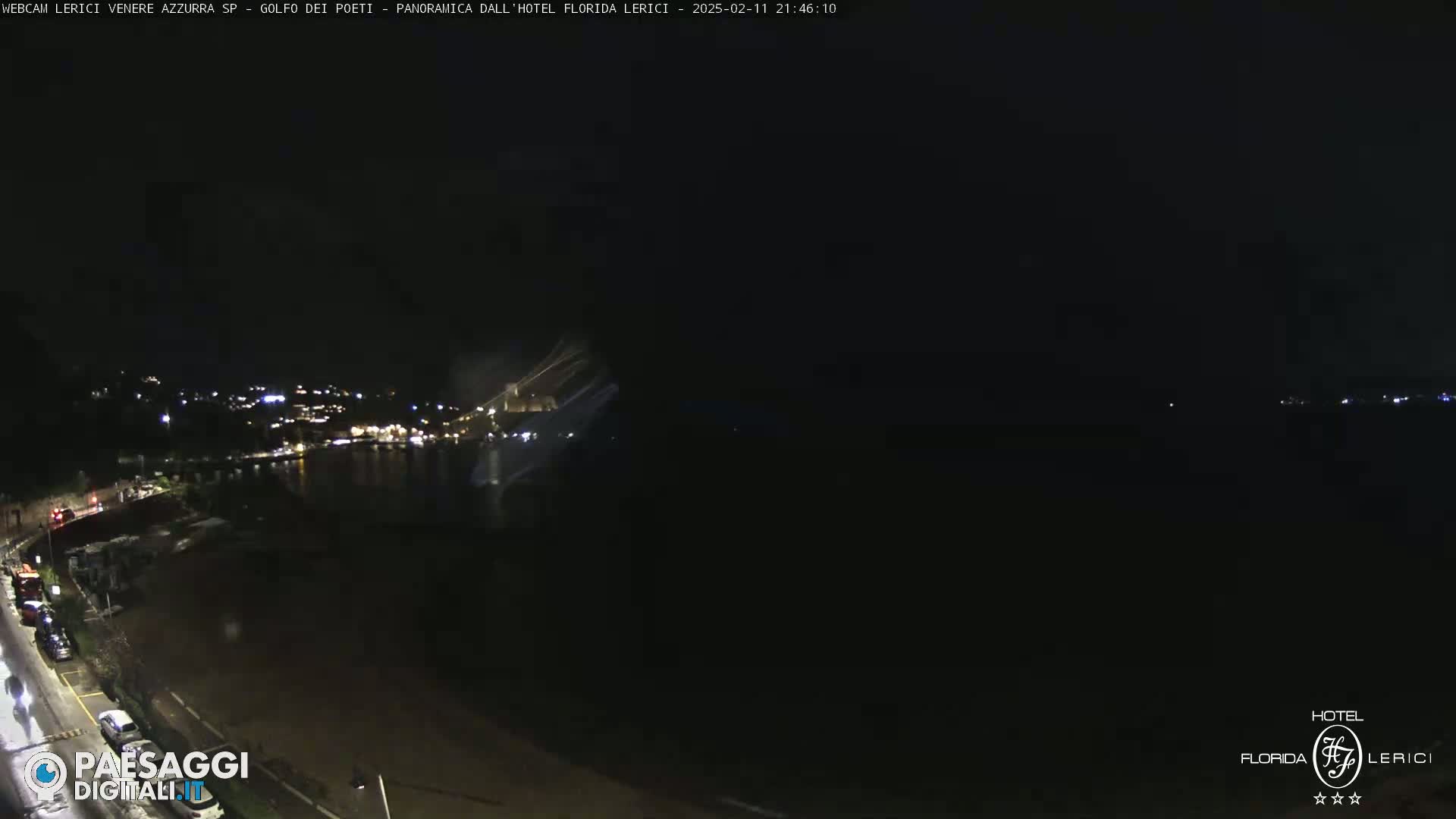 A nighttime coastal scene shows a dark body of water and a sparsely lit shoreline with parked cars.