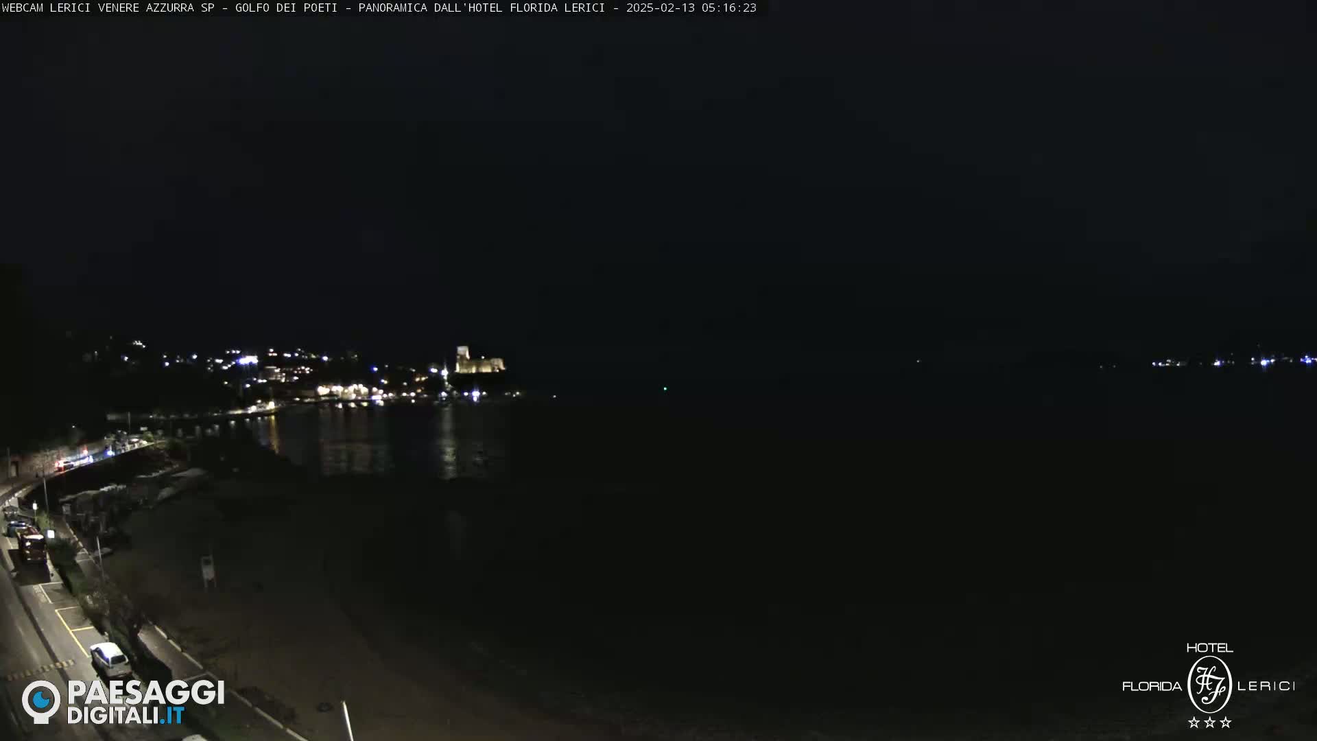 A nighttime coastal scene shows a dark body of water with a faintly lit town on the opposite shore.
