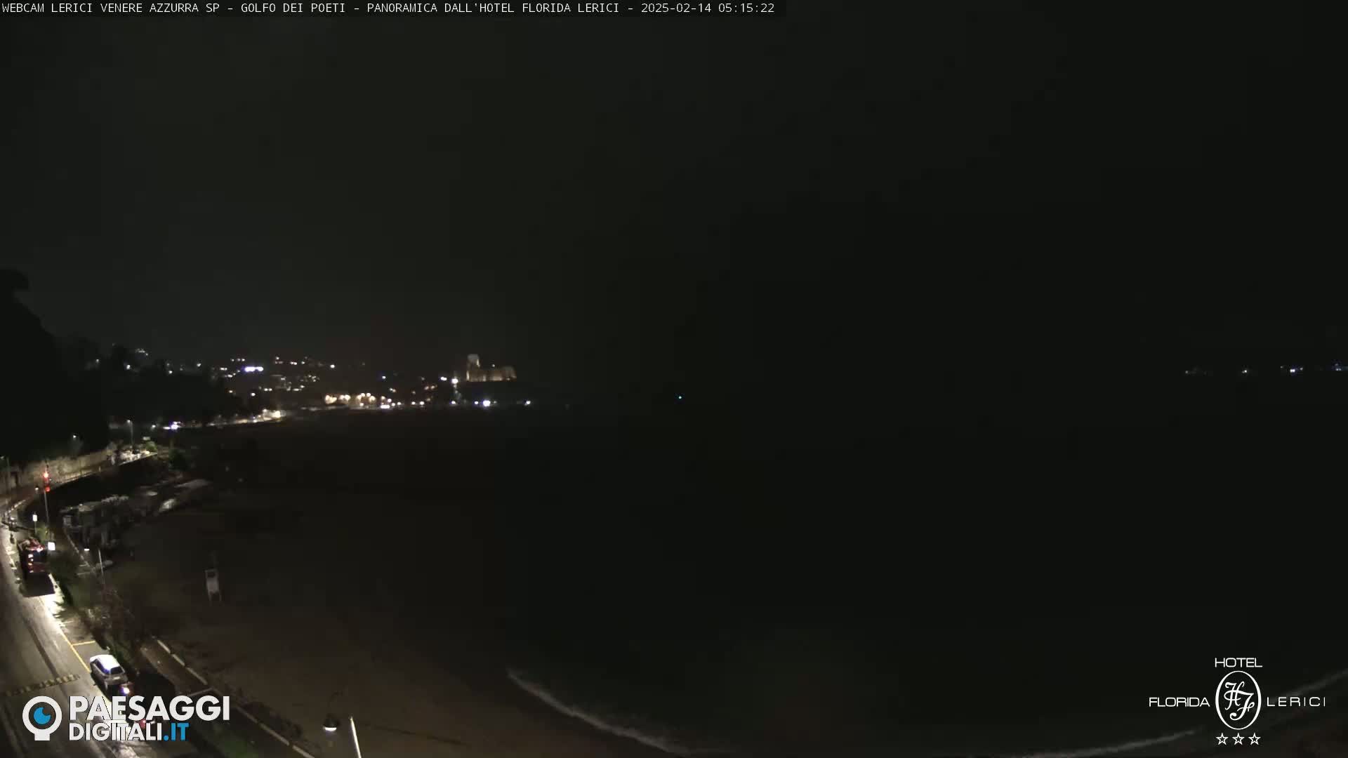 A dark nighttime coastal scene shows a sparsely lit town and beach with a dark ocean under a clear sky.