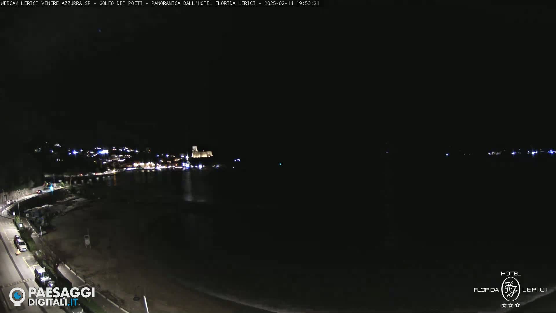 A nighttime view of a dark coastline with a few lights visible in the distance, and a calm, dark body of water in the foreground.