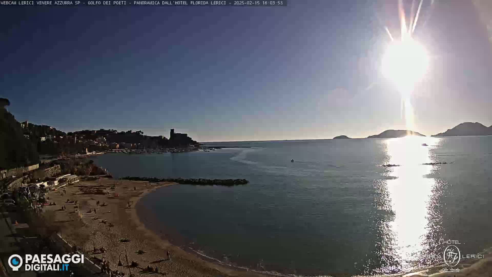 A sunny day at a sandy beach cove with calm water, overlooking a town and hills in the distance.
