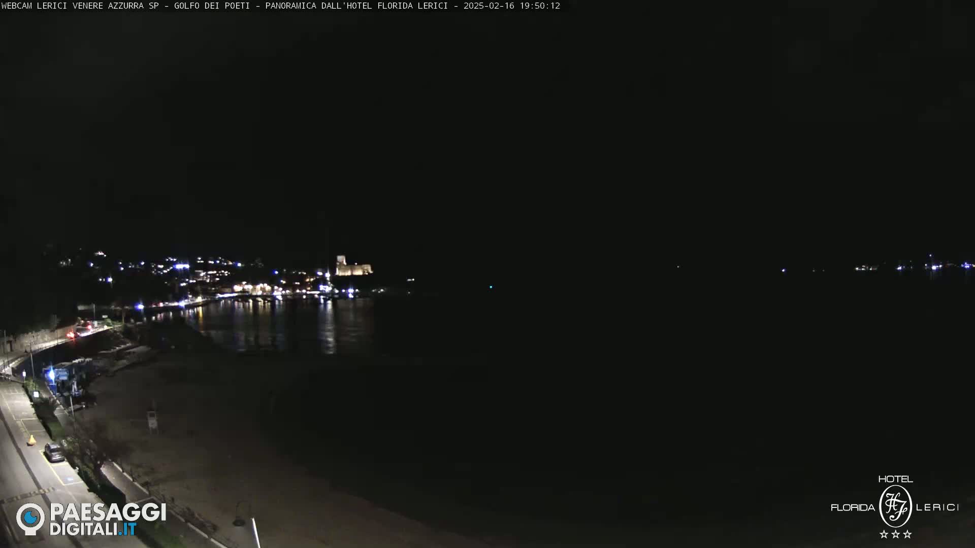 A nighttime, low-angle view of a dark coastline with a town's lights across a calm body of water.