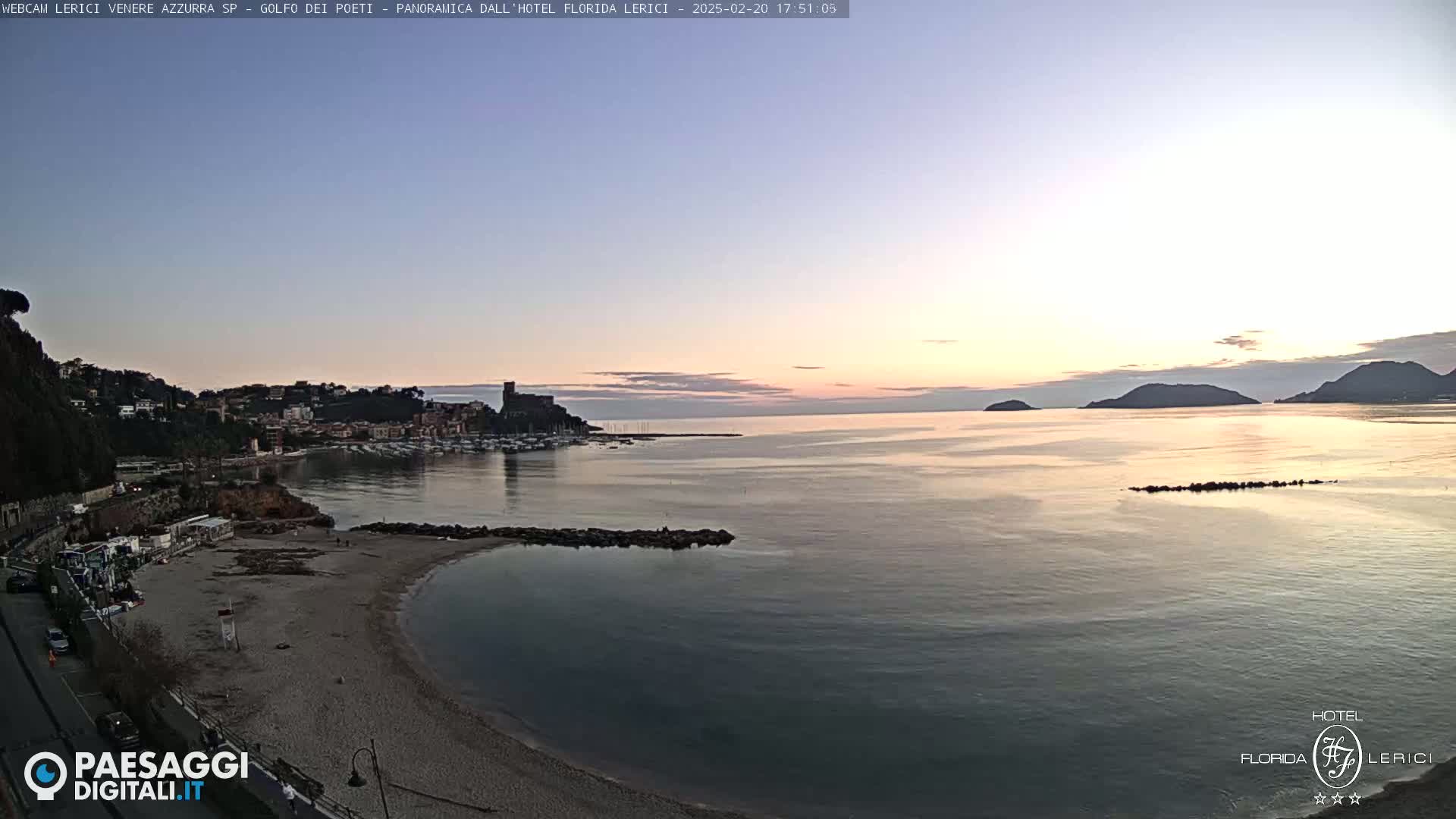 A tranquil coastal town at sunset, with a calm sea reflecting the soft light and a sandy beach stretching along the shoreline.