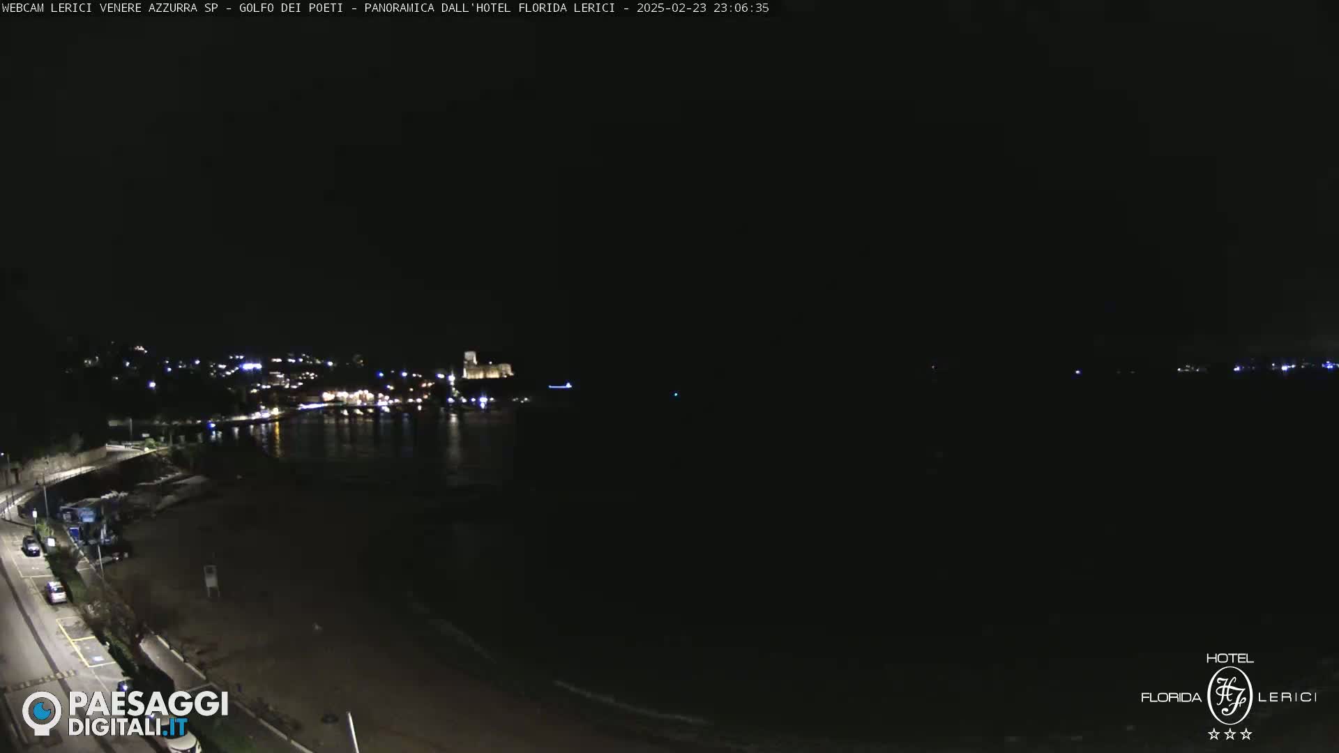 A nighttime coastal scene shows a dark beach and calm water, with a town's lights visible in the distance.