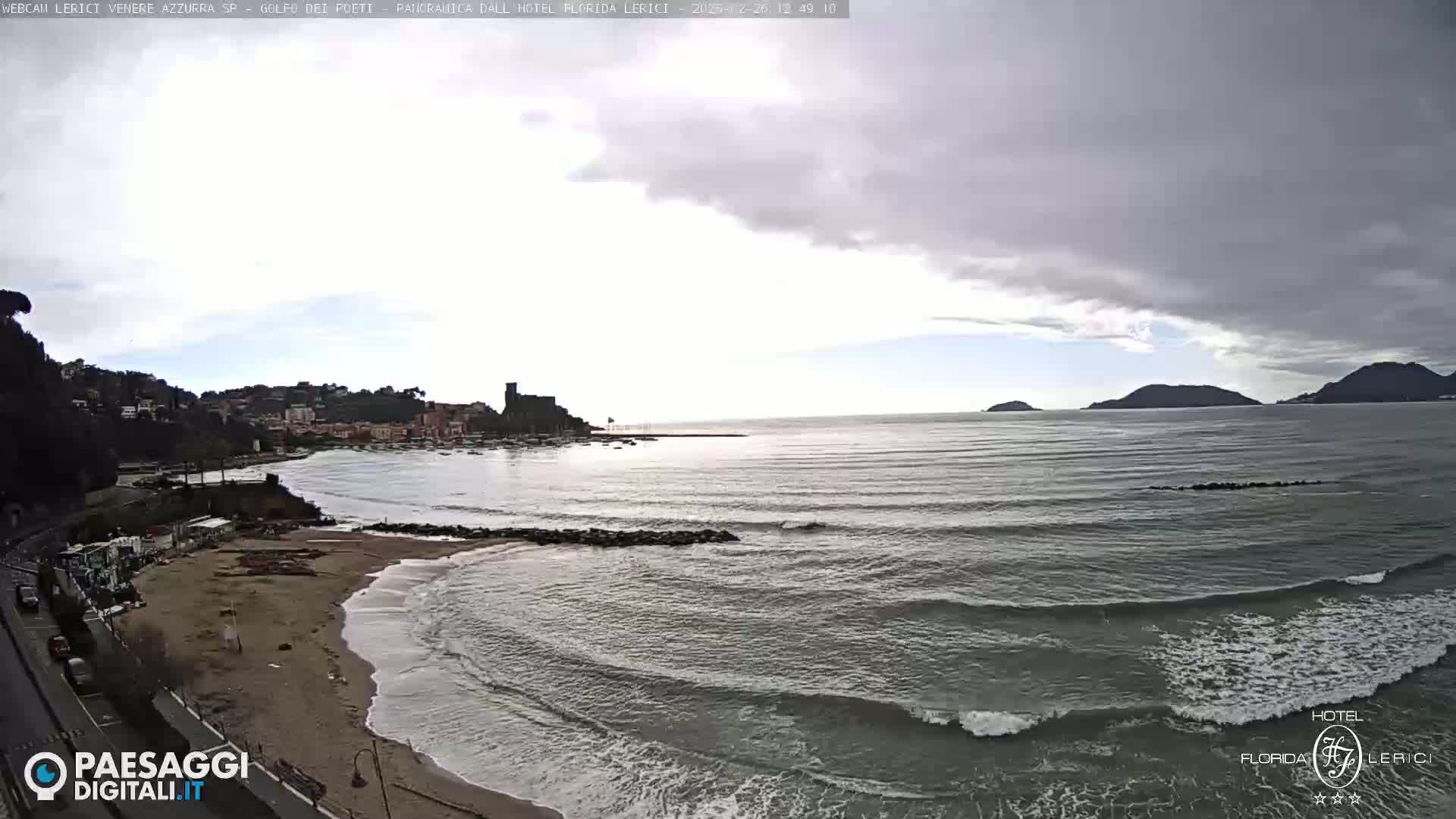 A coastal town with a sandy beach and calm ocean waves under a cloudy sky.