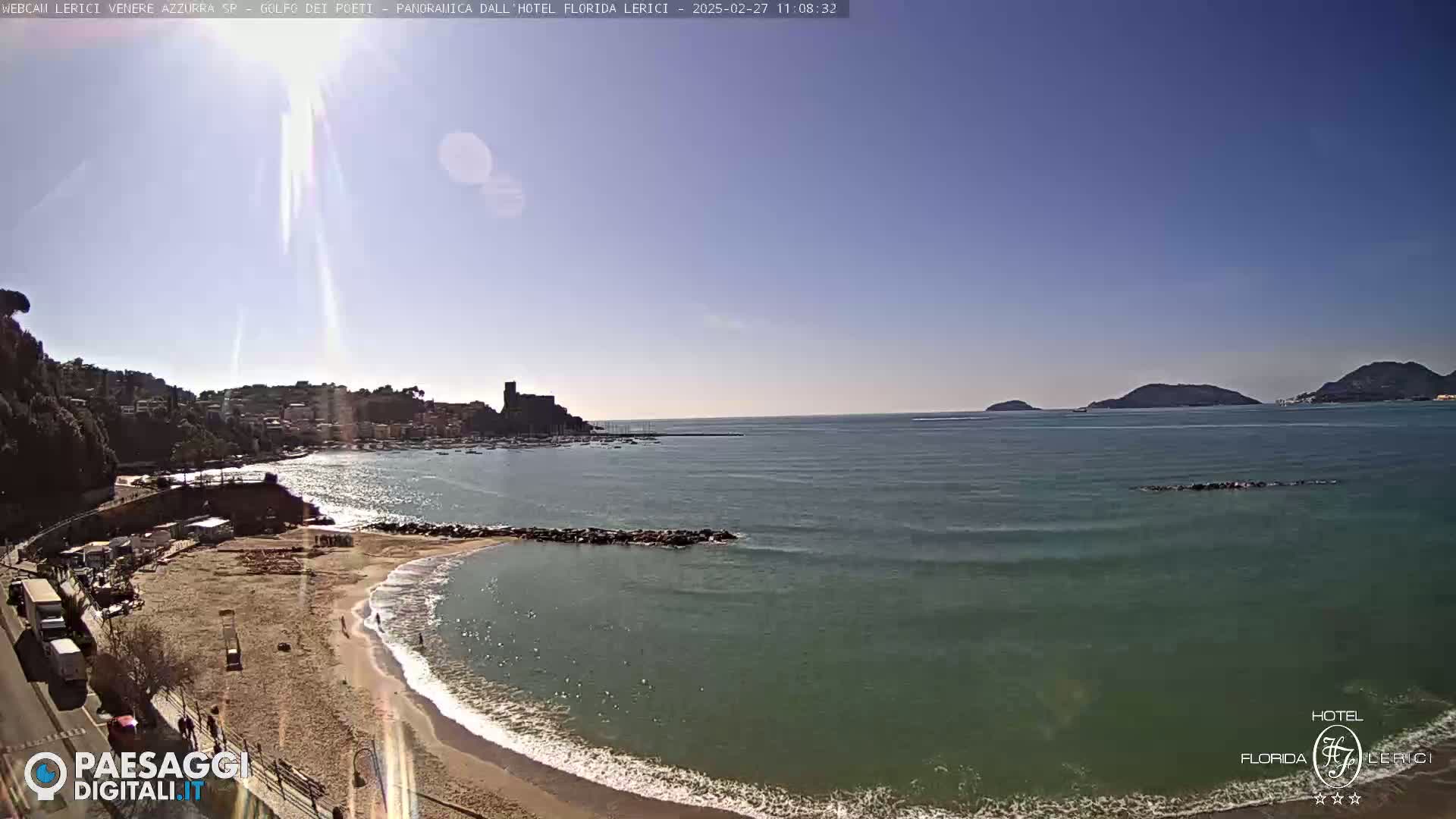 A sunny day overlooking a sandy beach, calm sea, and distant hills.