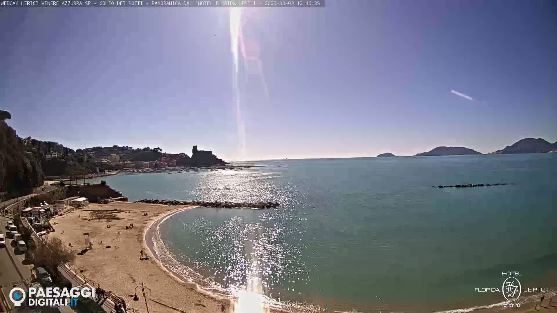 A sunny day at a sandy beach cove overlooking a calm sea with hills and a town in the background.