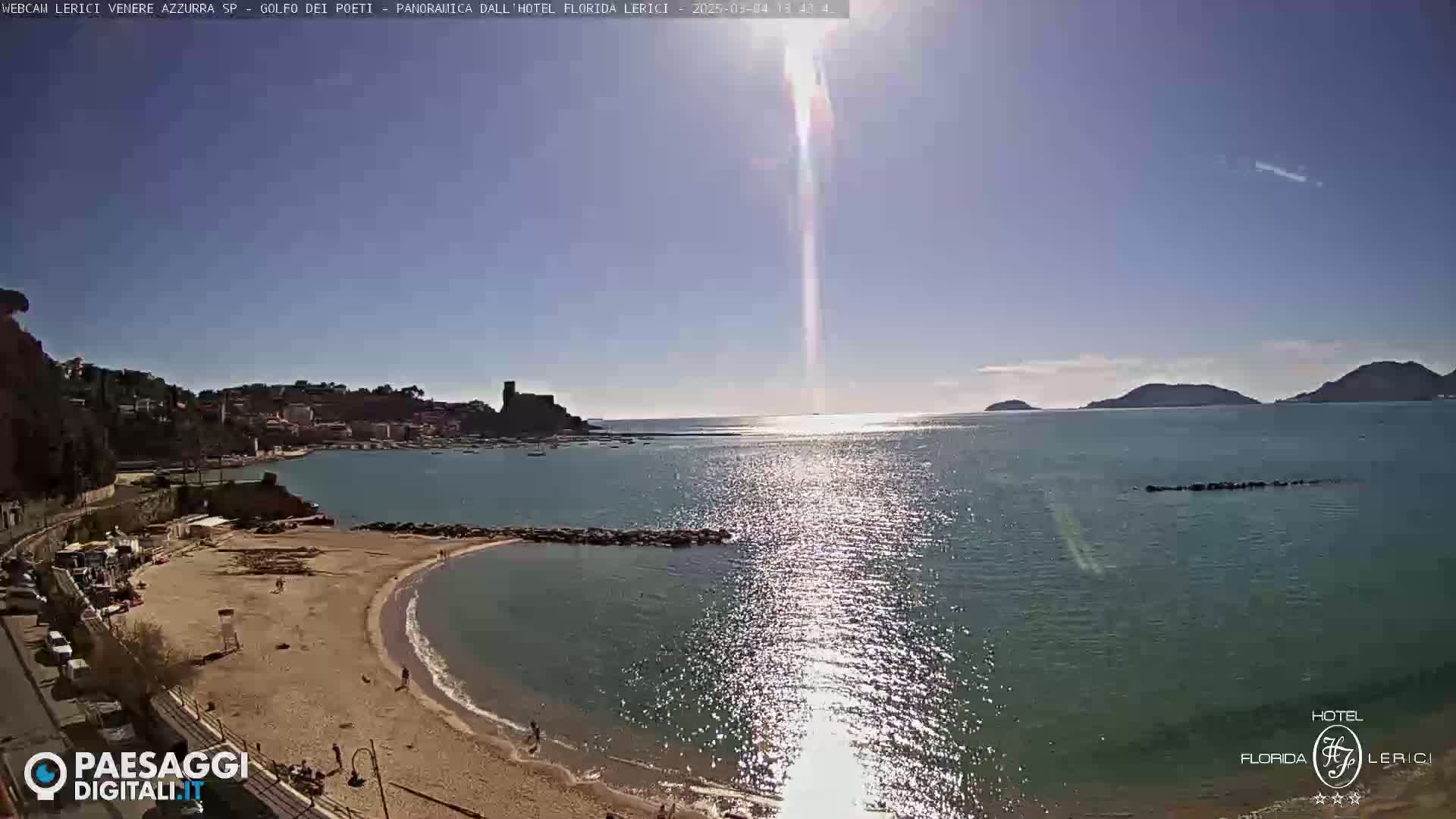 A sunny day at a sandy beach cove overlooking a calm bay with a town and hills in the distance.