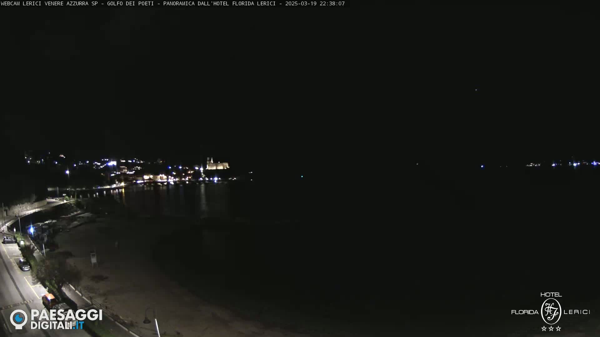 A nighttime, long shot of a dark beach and a town with lights across the water.