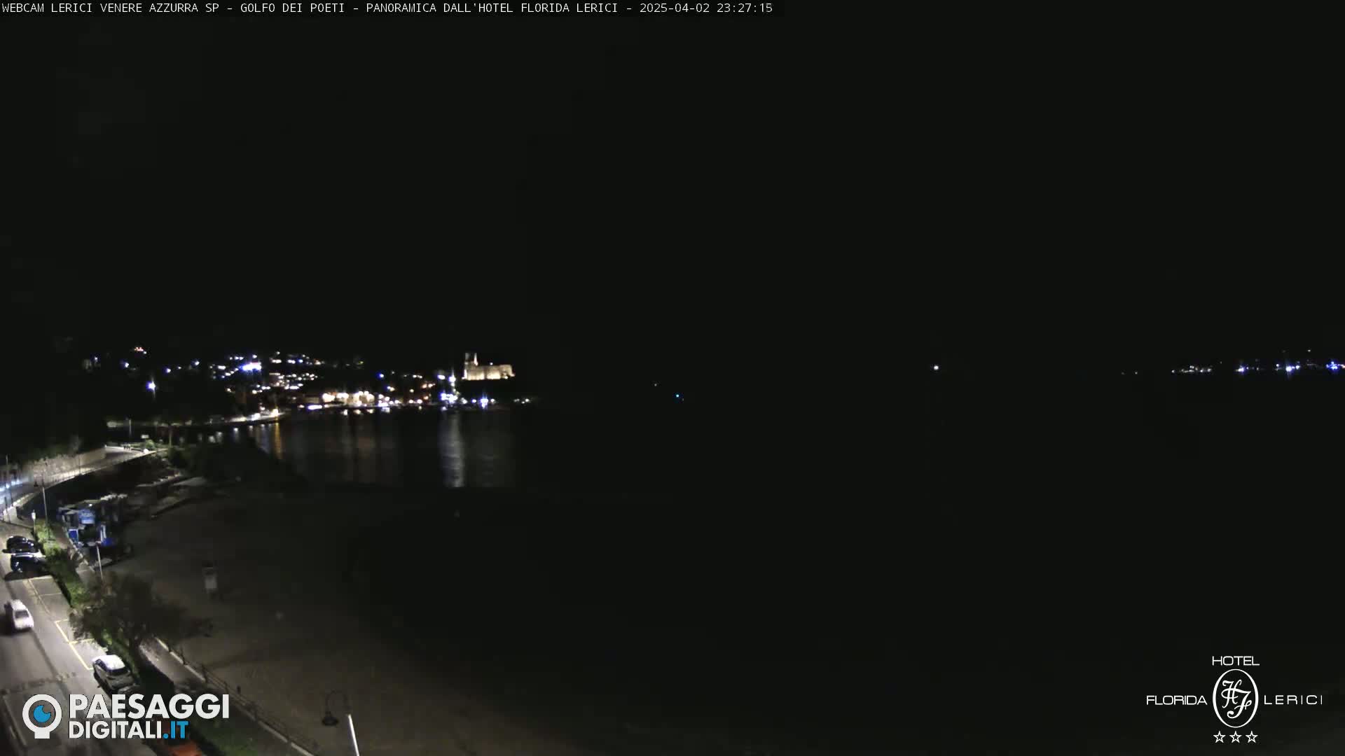A nighttime, long shot of a coastal town with lights visible across a dark body of water, under a clear, dark sky.
