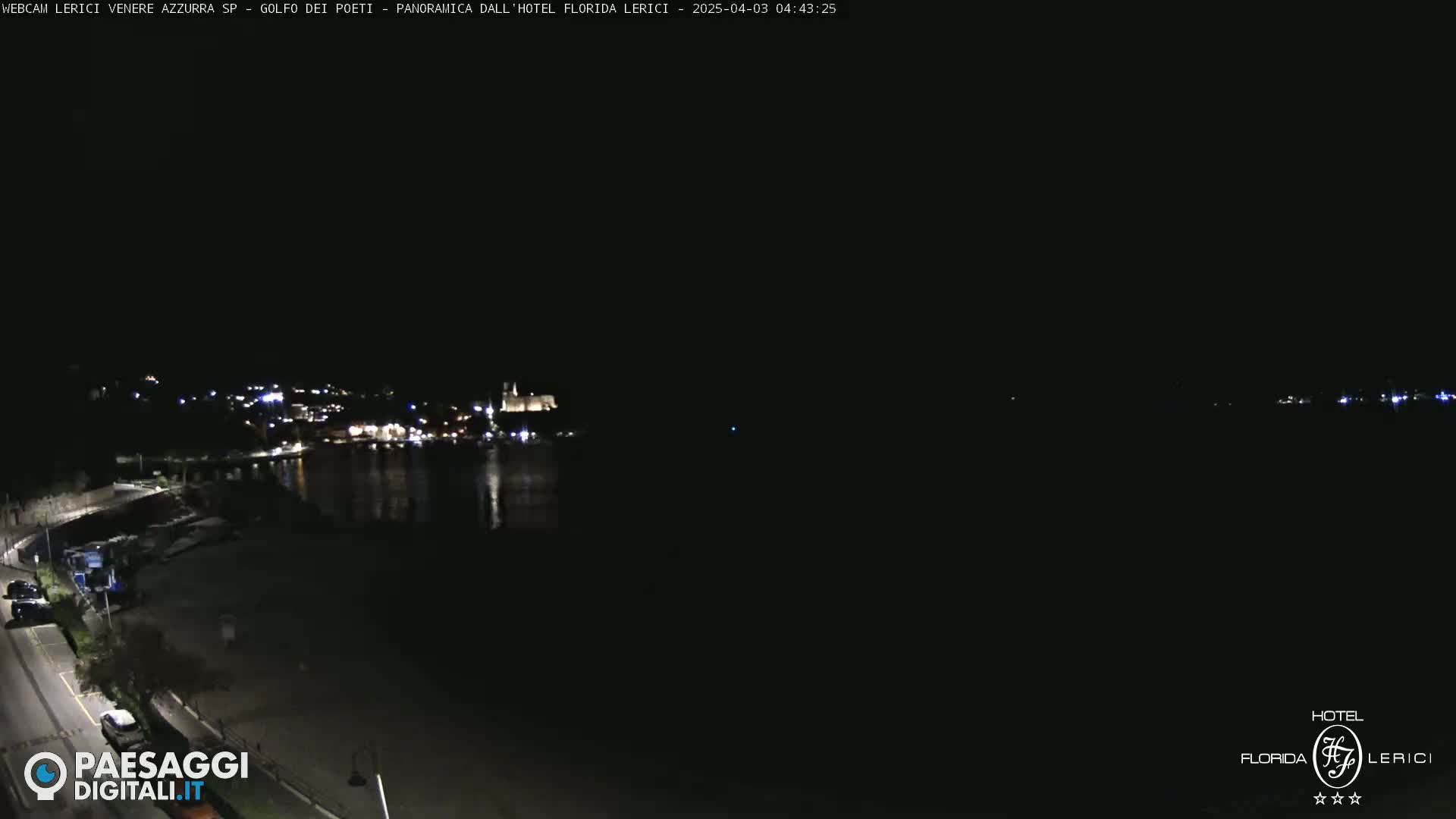A nighttime, long shot of a coastal town with its lights reflecting on dark water.