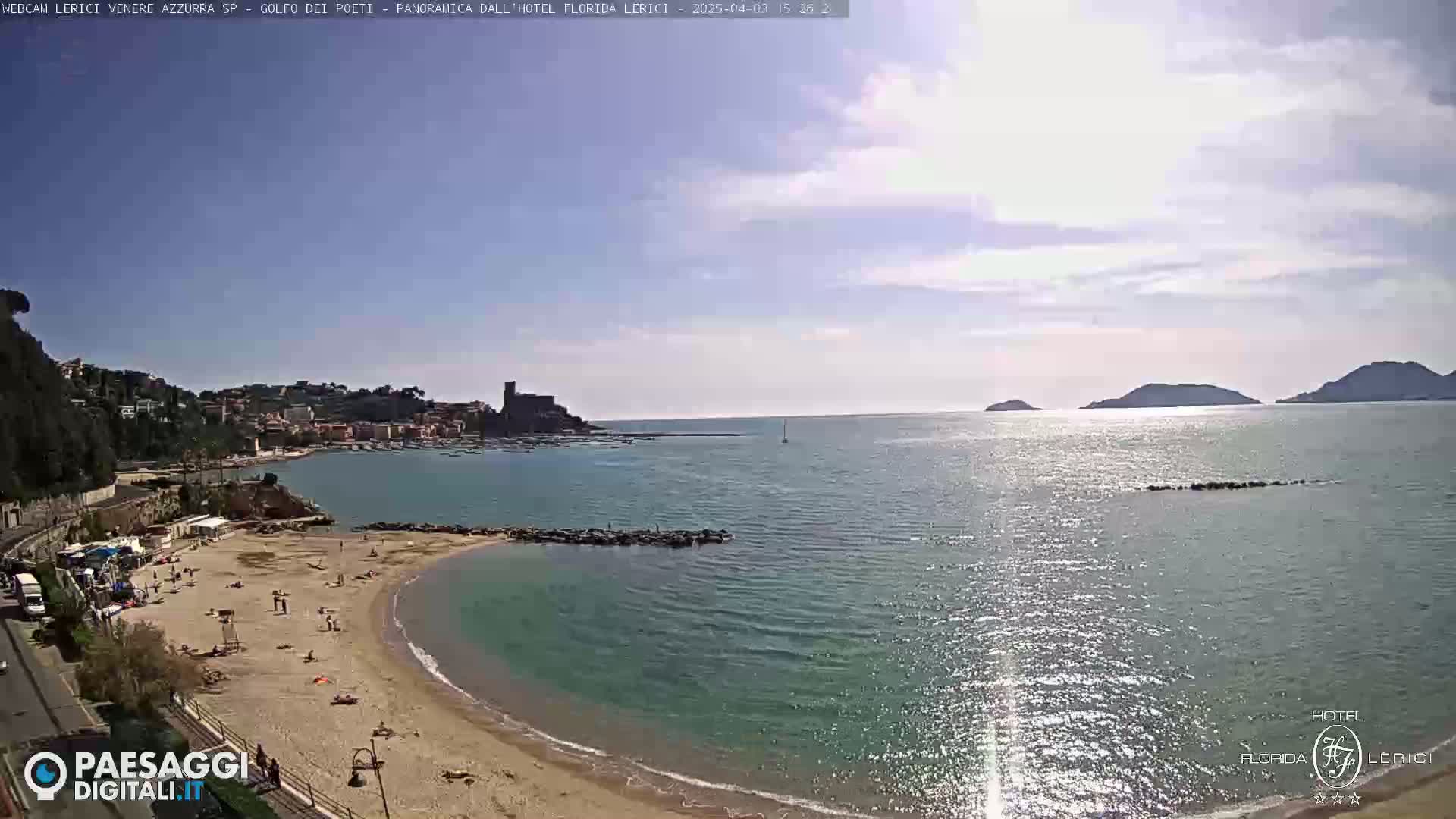 A partly sunny day at a sandy beach cove, with calm, sparkling turquoise water extending to a distant coastline and islands.