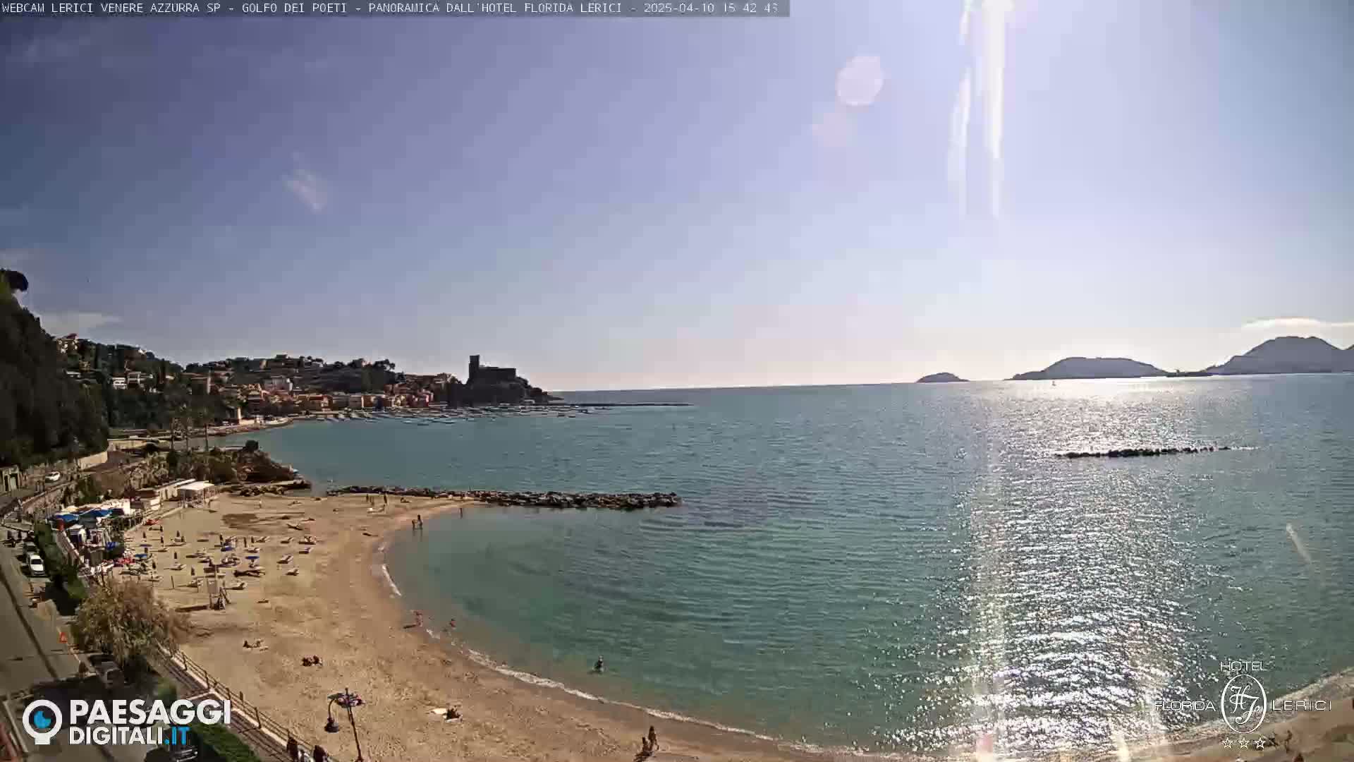 A sunny day at a sandy beach cove, overlooking a calm sea with a town and distant hills in the background.