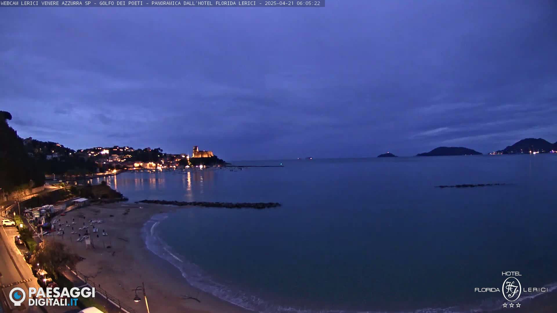 A dimly lit coastal town at twilight, with a sandy beach and calm sea, is nestled between hills under a dusky sky.