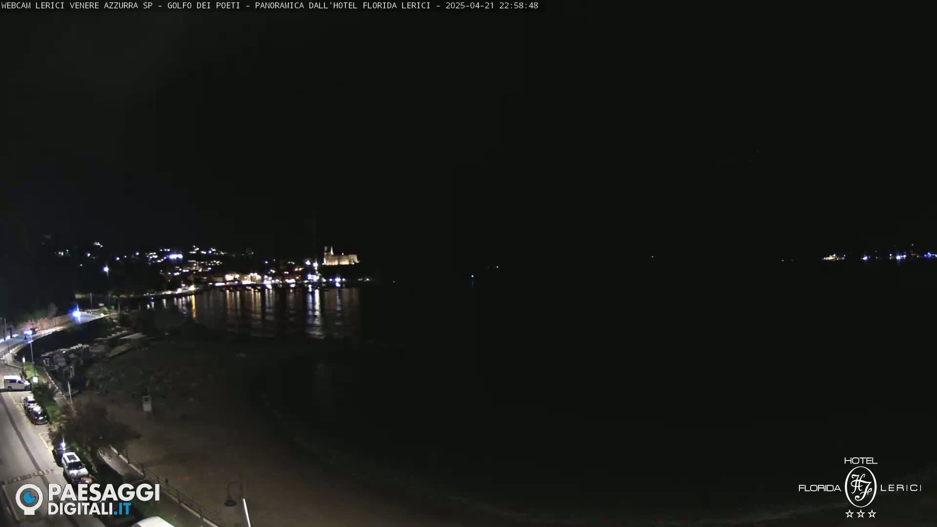 A nighttime view of a dark coastline with a town's lights reflecting on the water.
