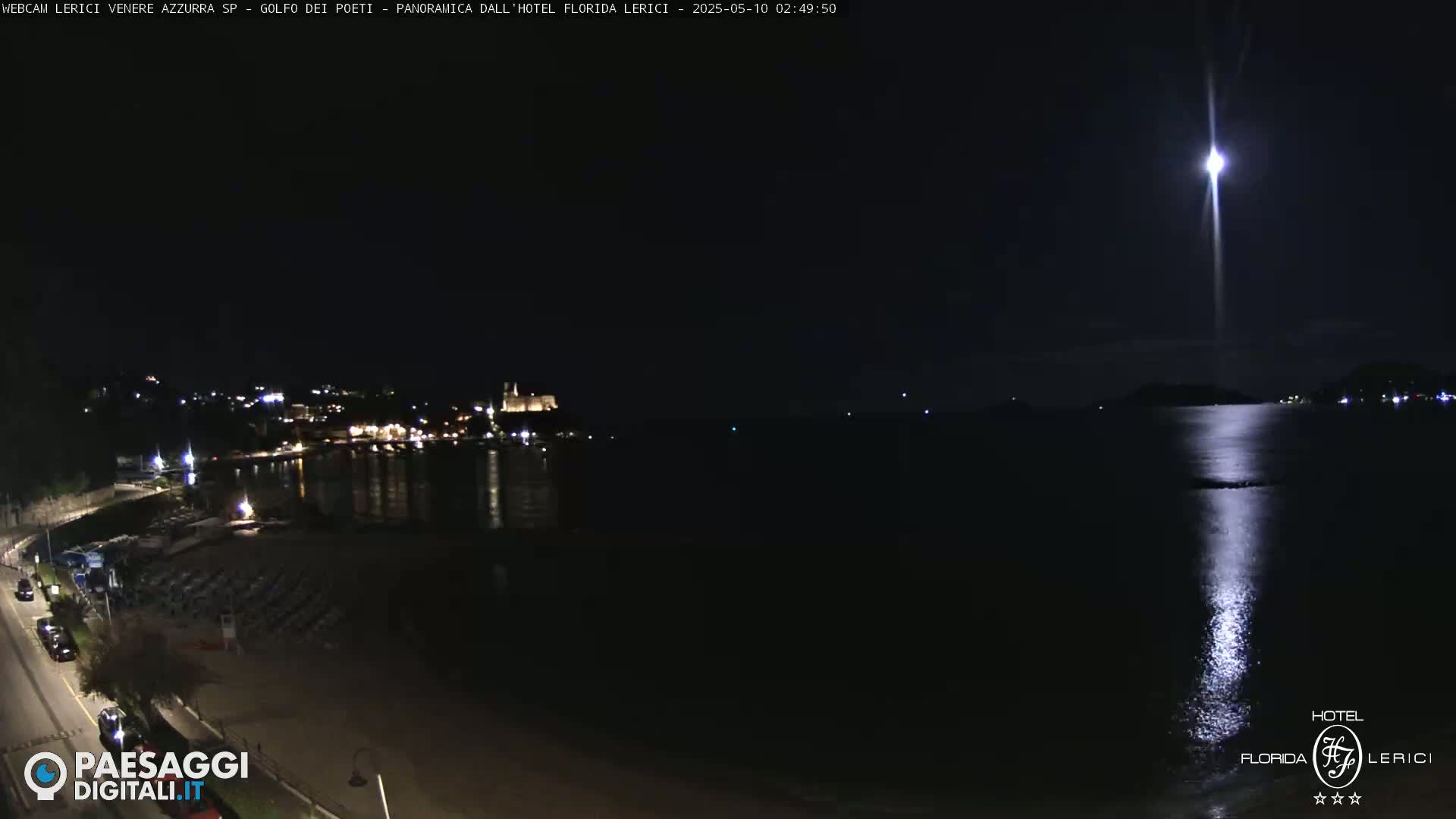 A nighttime coastal scene shows a moonlit beach with a town and calm water reflecting the bright moon.