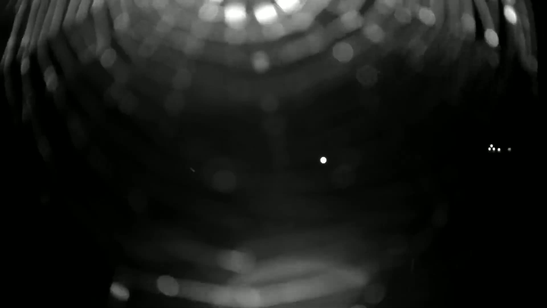 A blurry black and white image shows out-of-focus lights and particles, possibly snow.