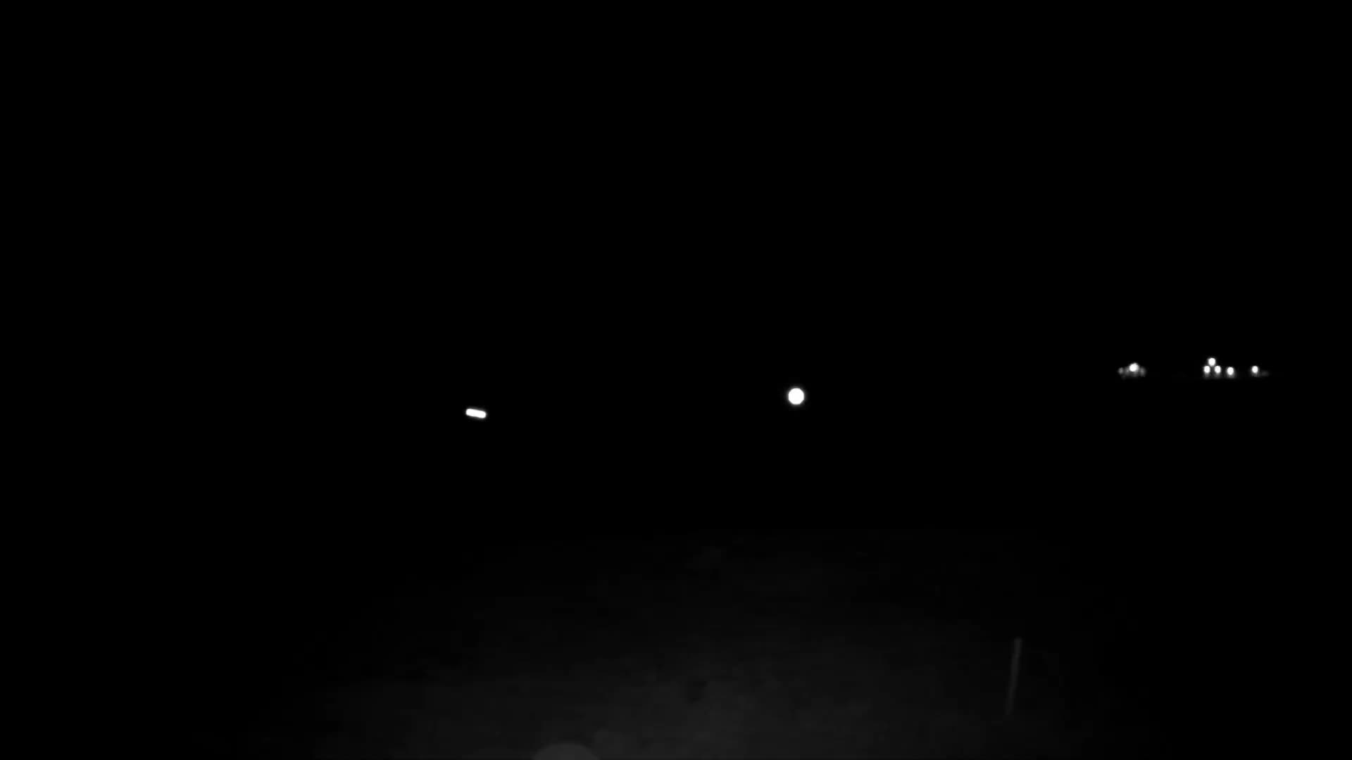 A clear, very dark night scene features several scattered bright white lights in the distance, with the ground barely discernible below.