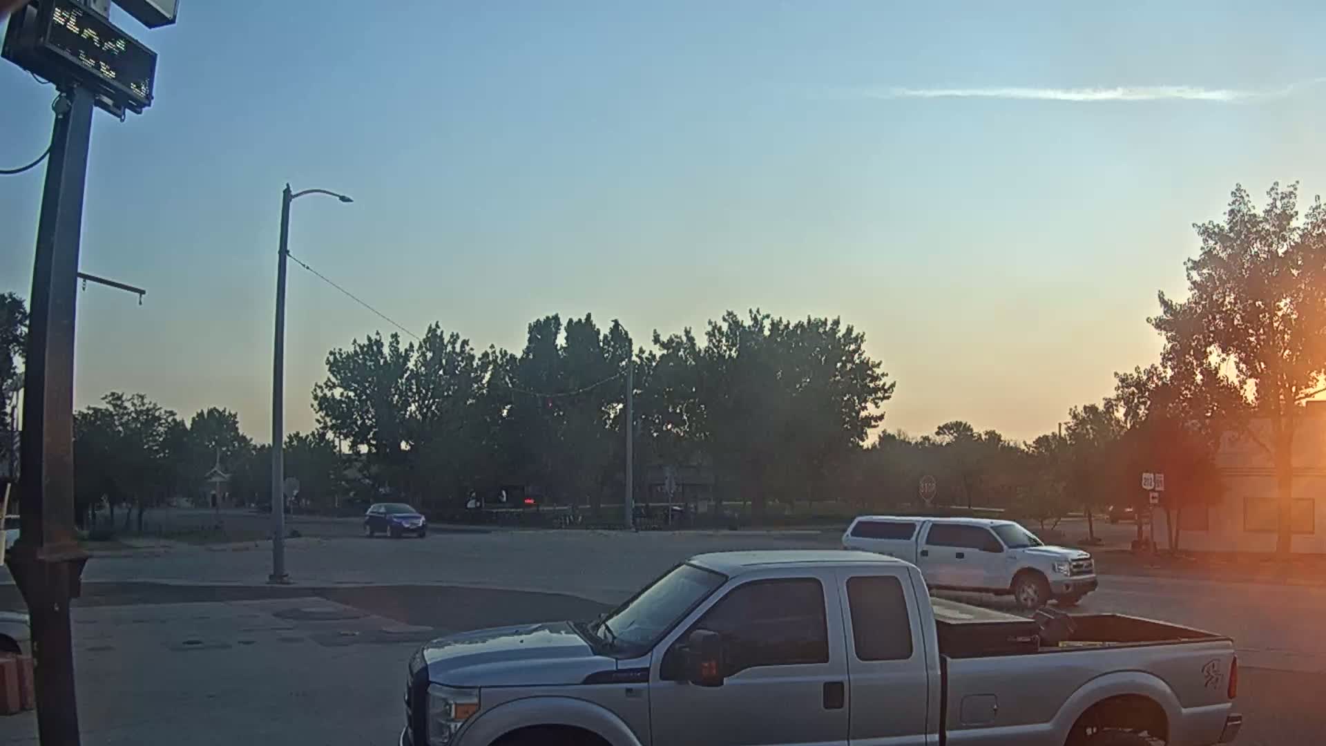 A nighttime view of a dimly lit intersection with streetlights, some trees, and a few vehicles visible in the distance under a hazy sky.