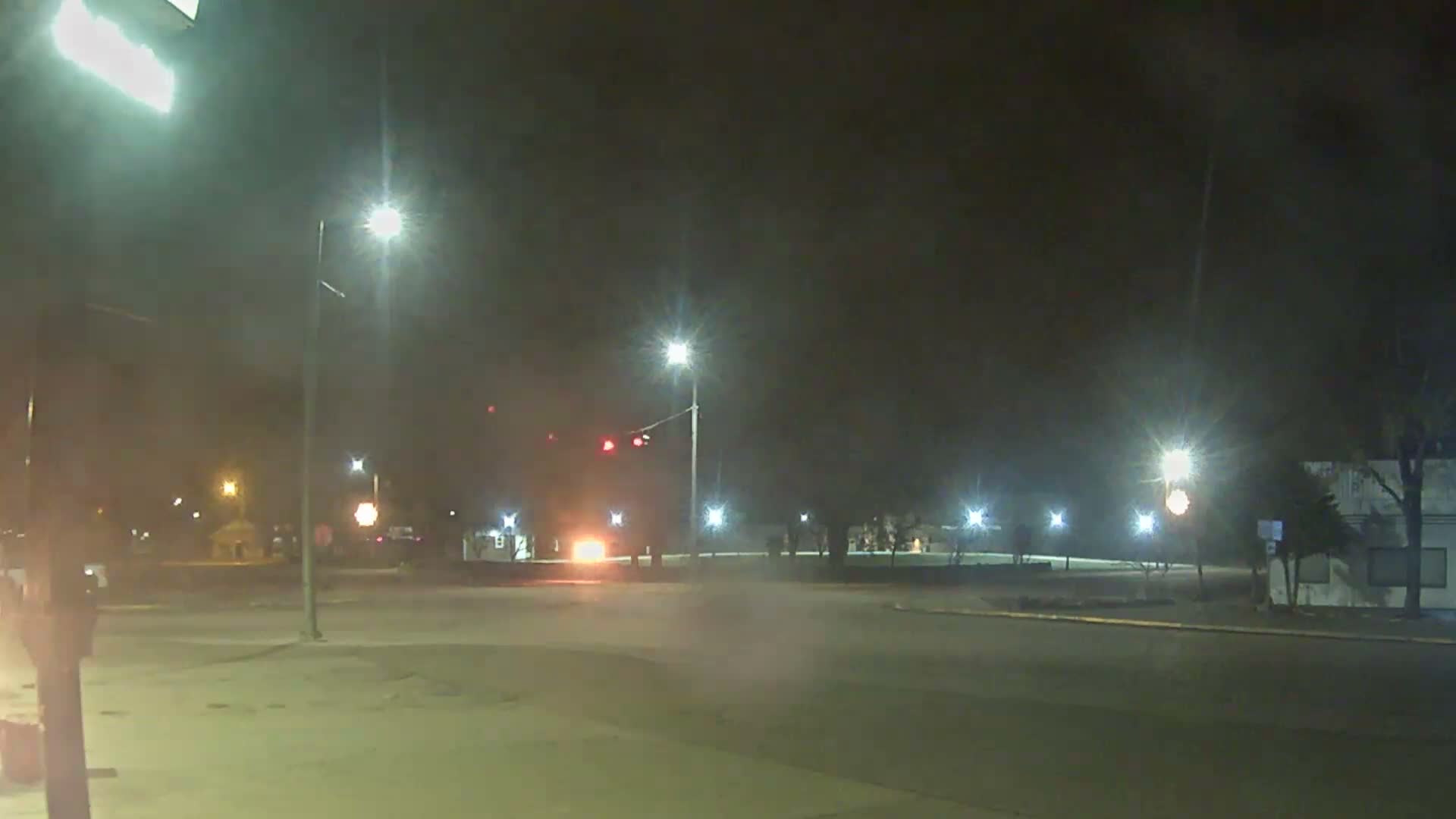 A clear night illuminates an empty urban intersection with numerous bright streetlights and distant building lights under a dark sky.