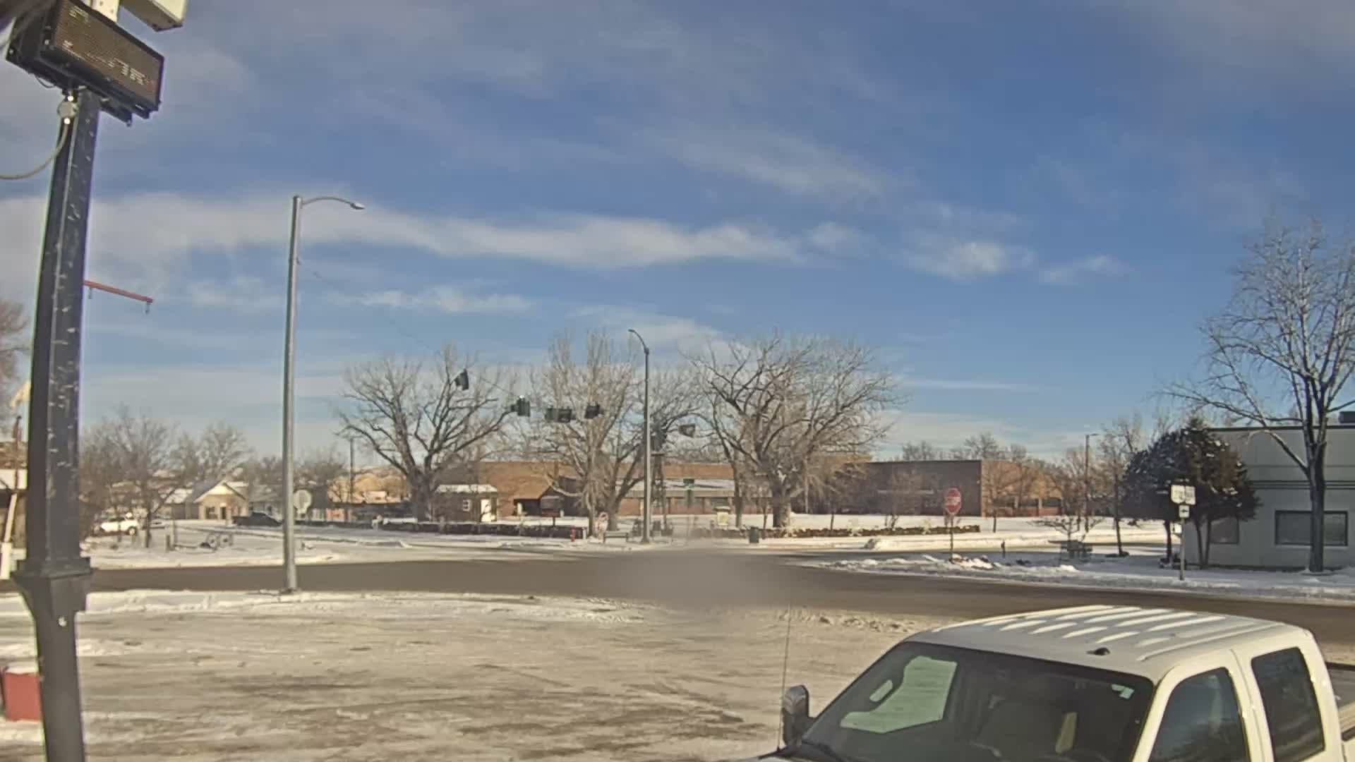 A wet and hazy night reveals a town square or intersection illuminated by streetlights, red traffic signals, and numerous festive holiday lights decorating the ground and buildings.
