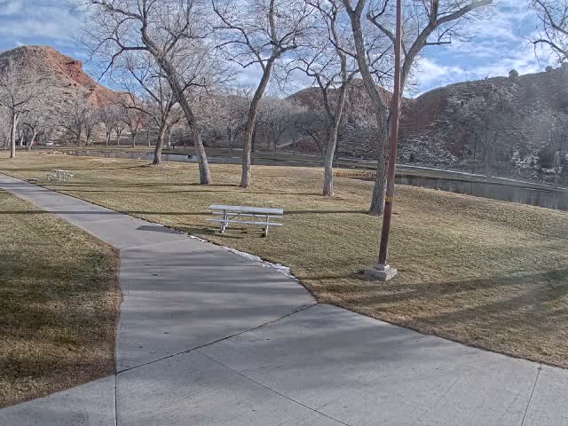 A concrete path winds through a park with snow-dusted ground and bare trees, illuminated by streetlights on a clear, cold night.