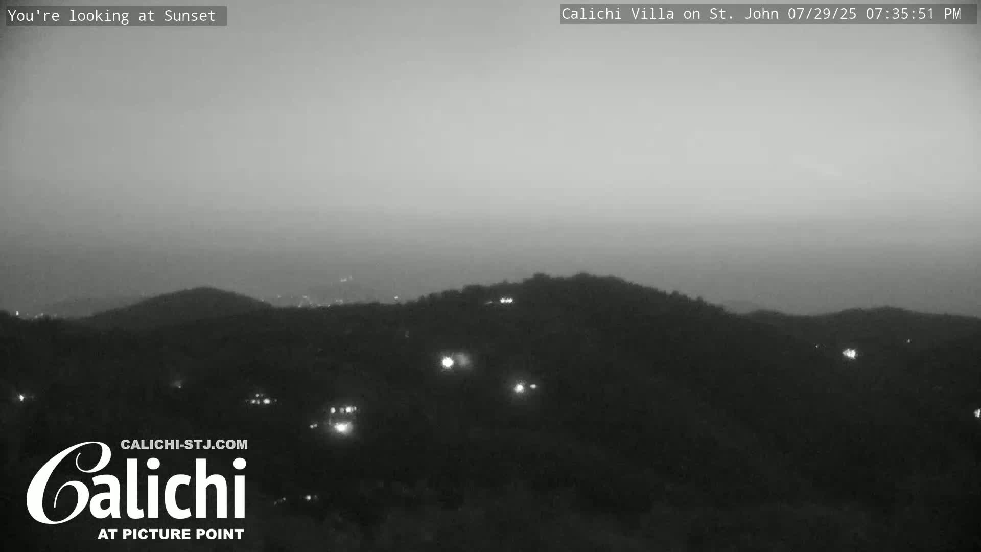 A nighttime, wide shot of a town with scattered lights under a cloudy sky.