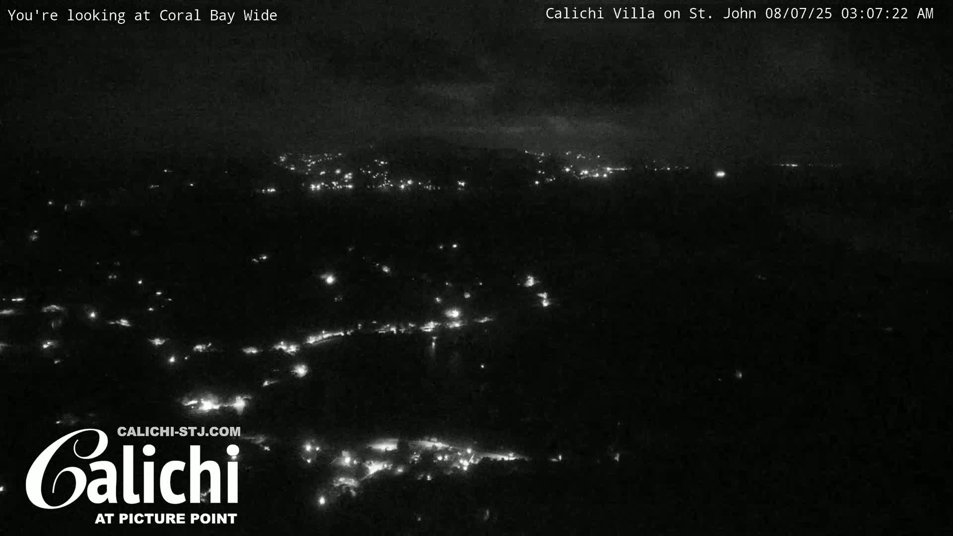 A nighttime, wide shot shows a dark landscape speckled with small, distant lights under a mostly cloudy sky.