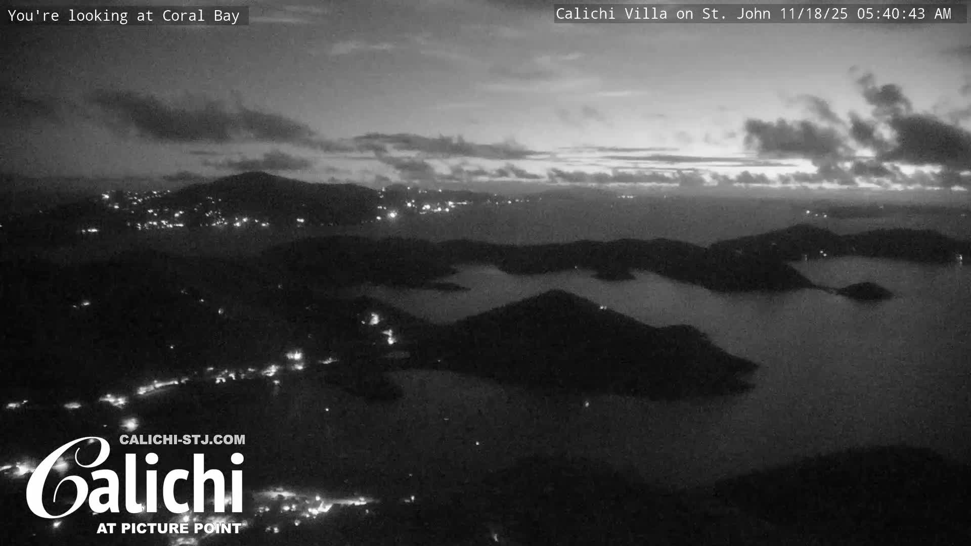A dark, clear night scene reveals scattered artificial lights from a coastal settlement illuminating a shoreline across a dark expanse of water.