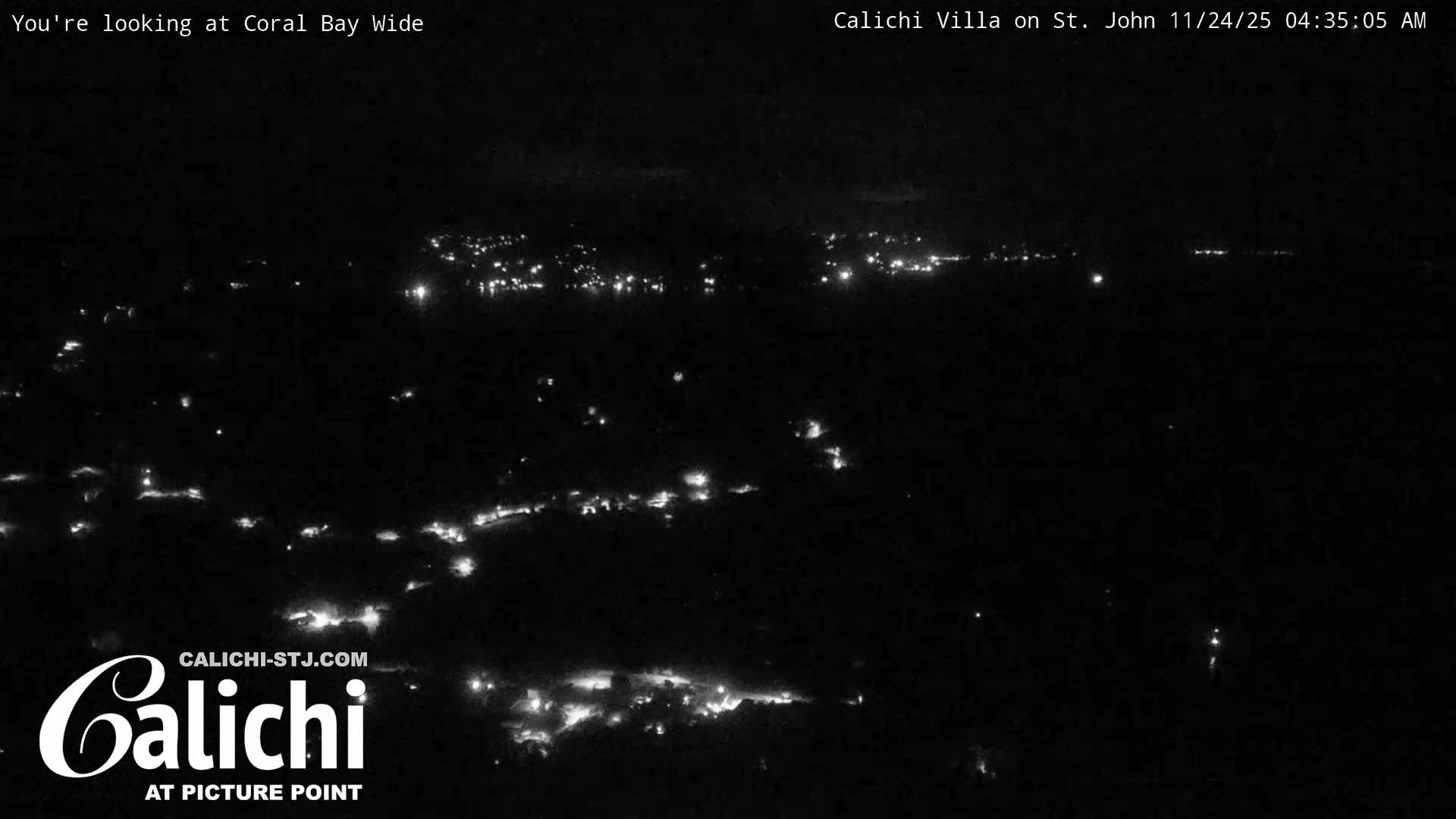 The image captures a wide view of a coastal settlement at night, with numerous artificial lights illuminating the landscape under clear skies.