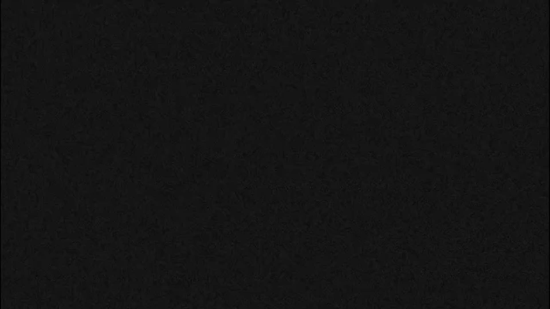 A dark, clear, and calm night view captures a blue boat docked in still water, partially obscured by green palm fronds, alongside a building with roof and lights on the right.